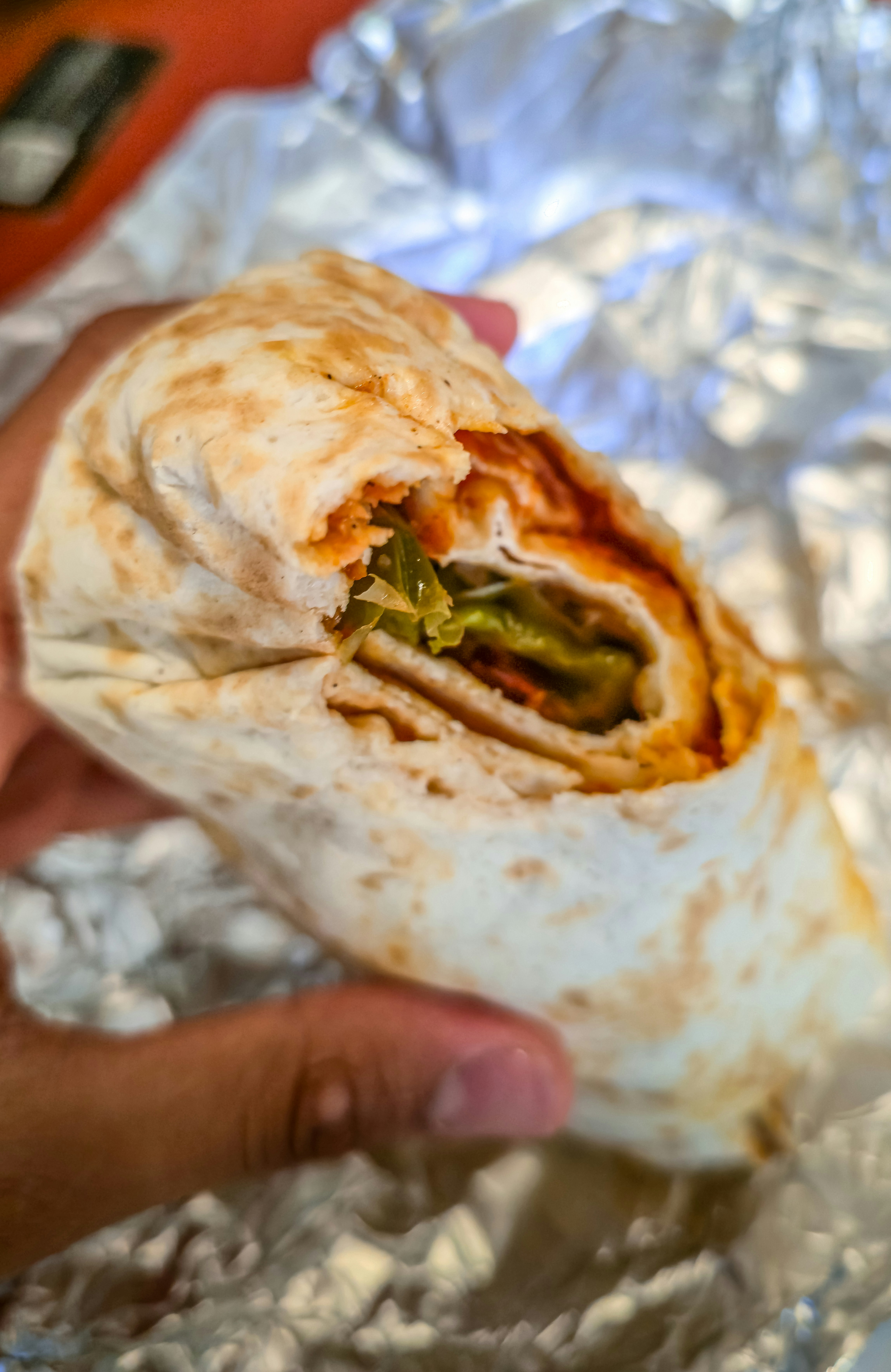 A hand holding a toasted tortilla wrap filled with vegetables and sauce