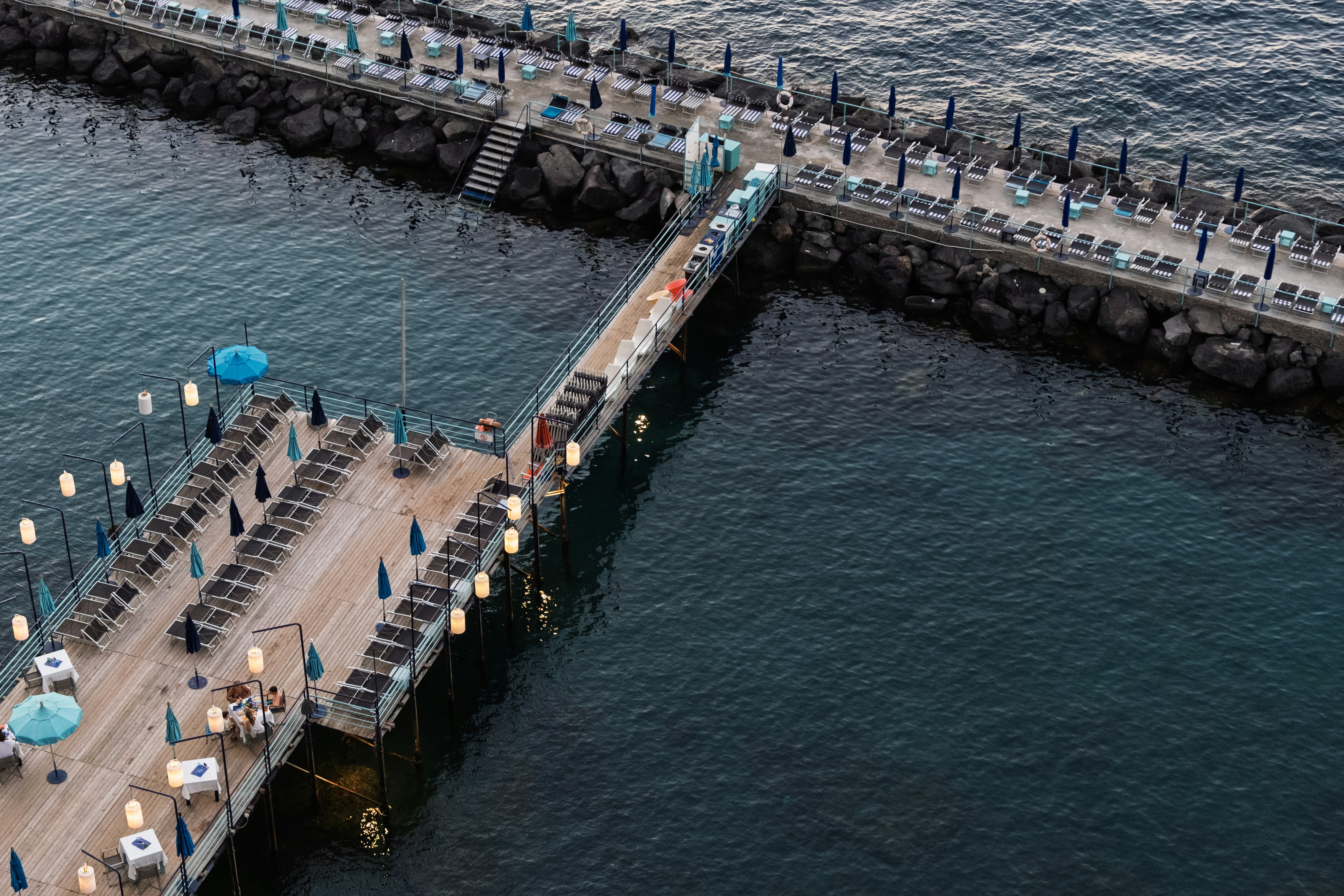Aerial view of a wooden pier with lounge chairs and umbrellas over dark water