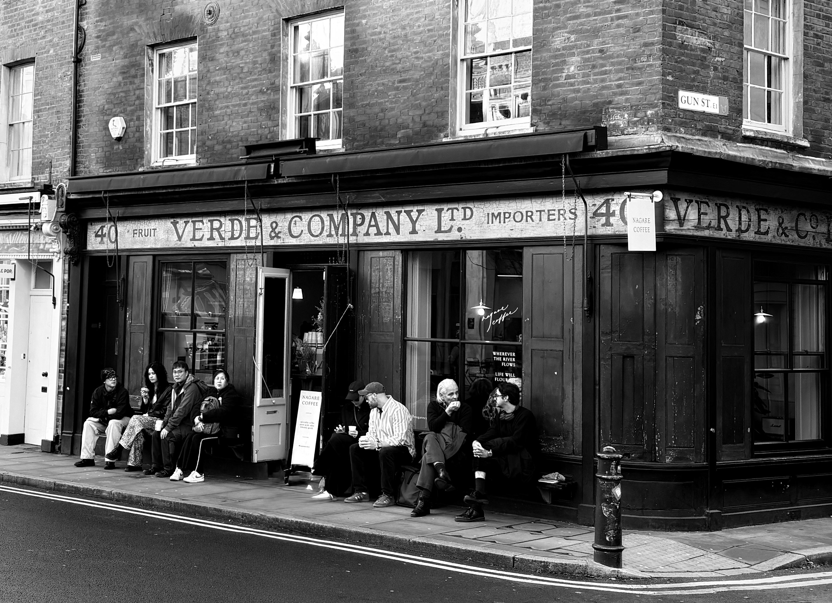 People sitting on a bench outside a brick storefront on Gun Street