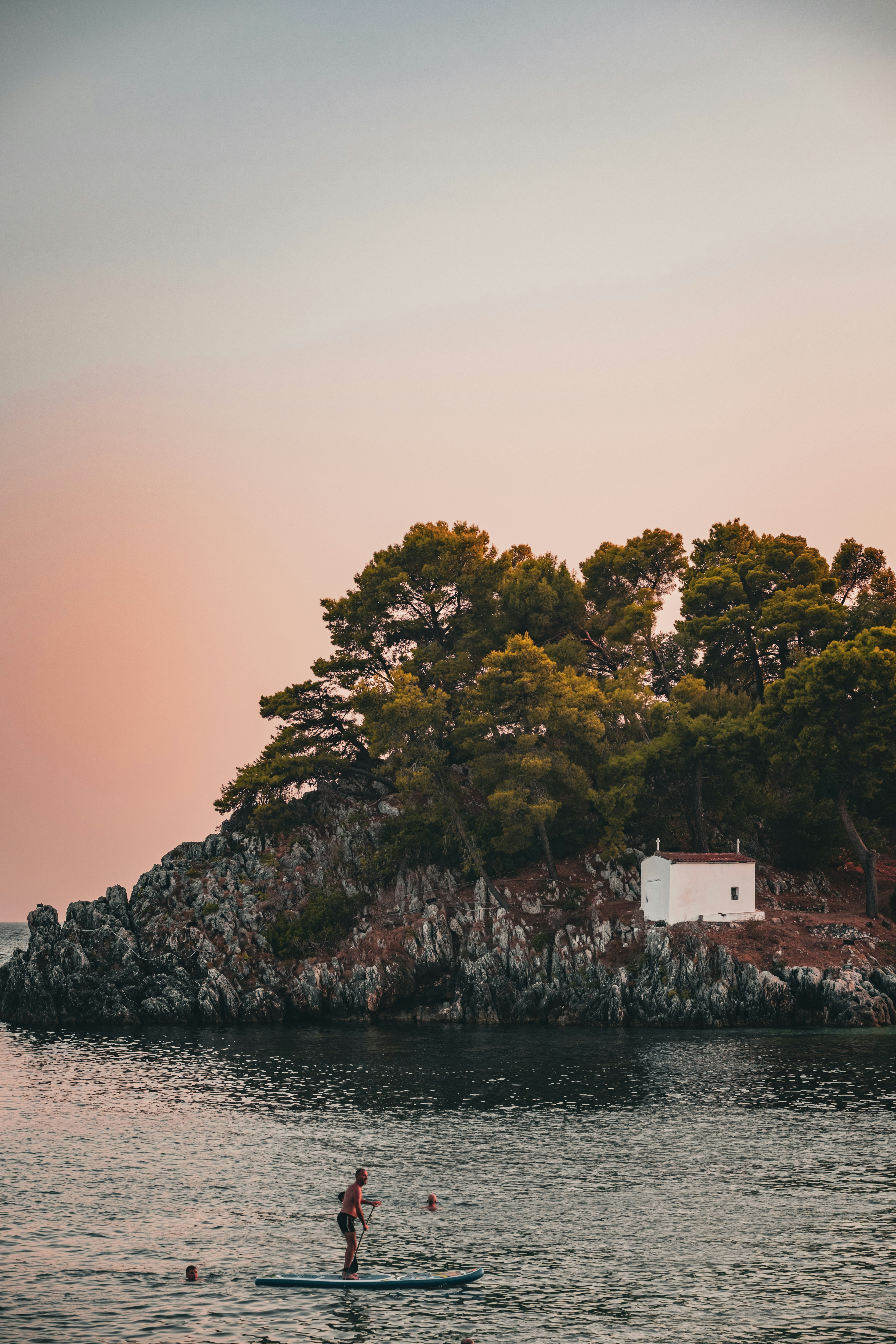 A person paddleboarding near a rocky island with a small white chapel and pine trees