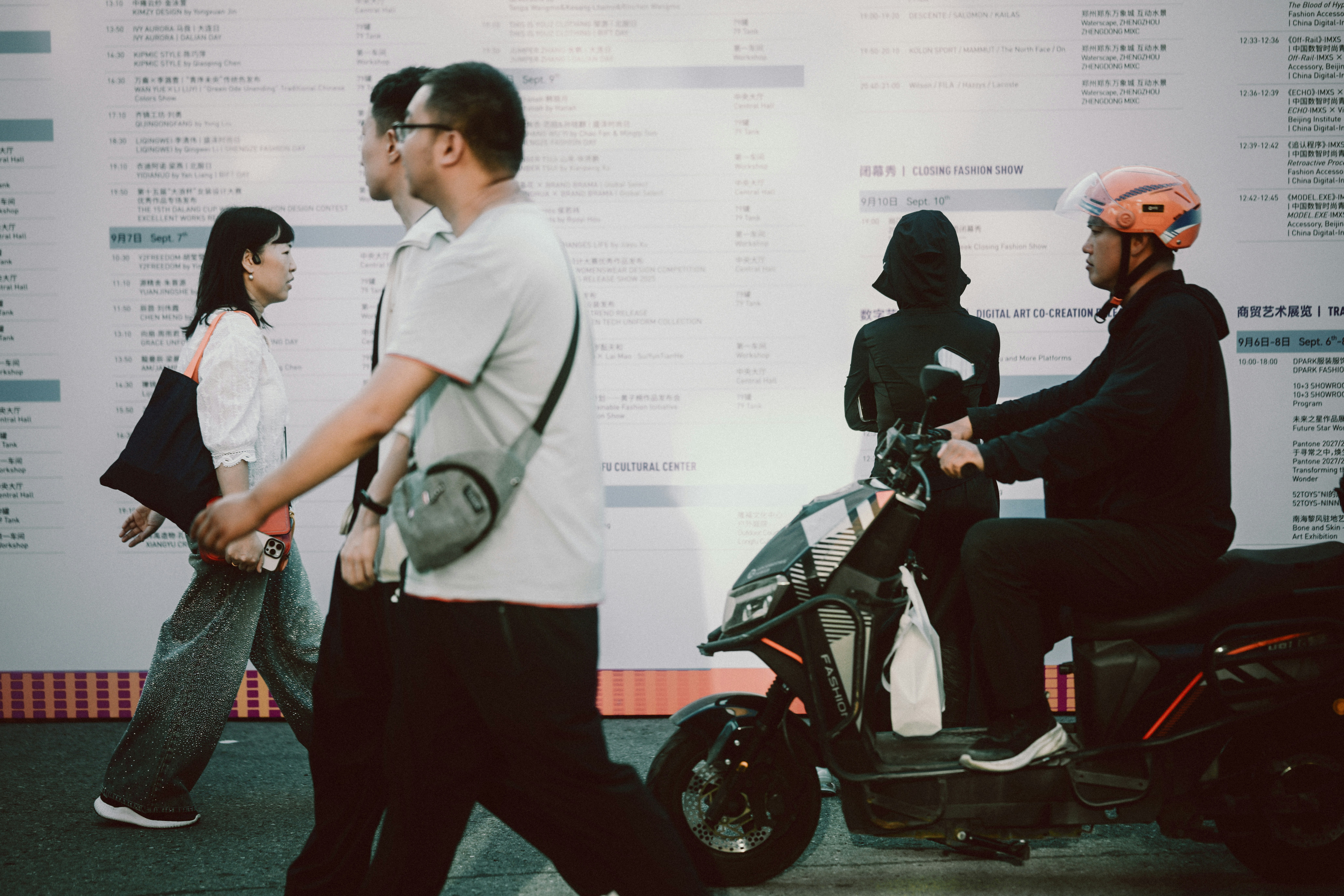 People walking past a person on a scooter in front of a schedule board