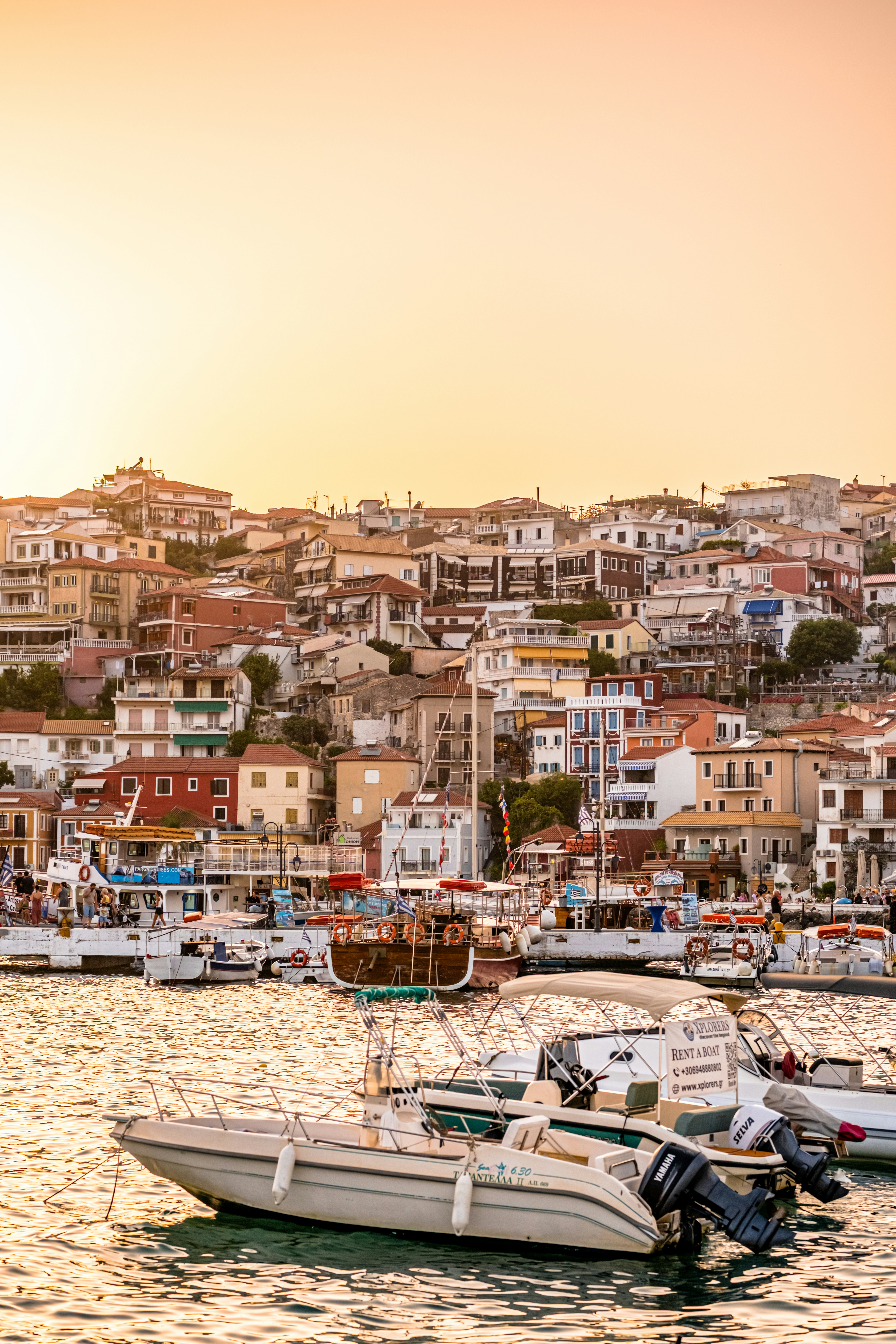Boats moored at a harbor in Parga with hillside houses under golden light