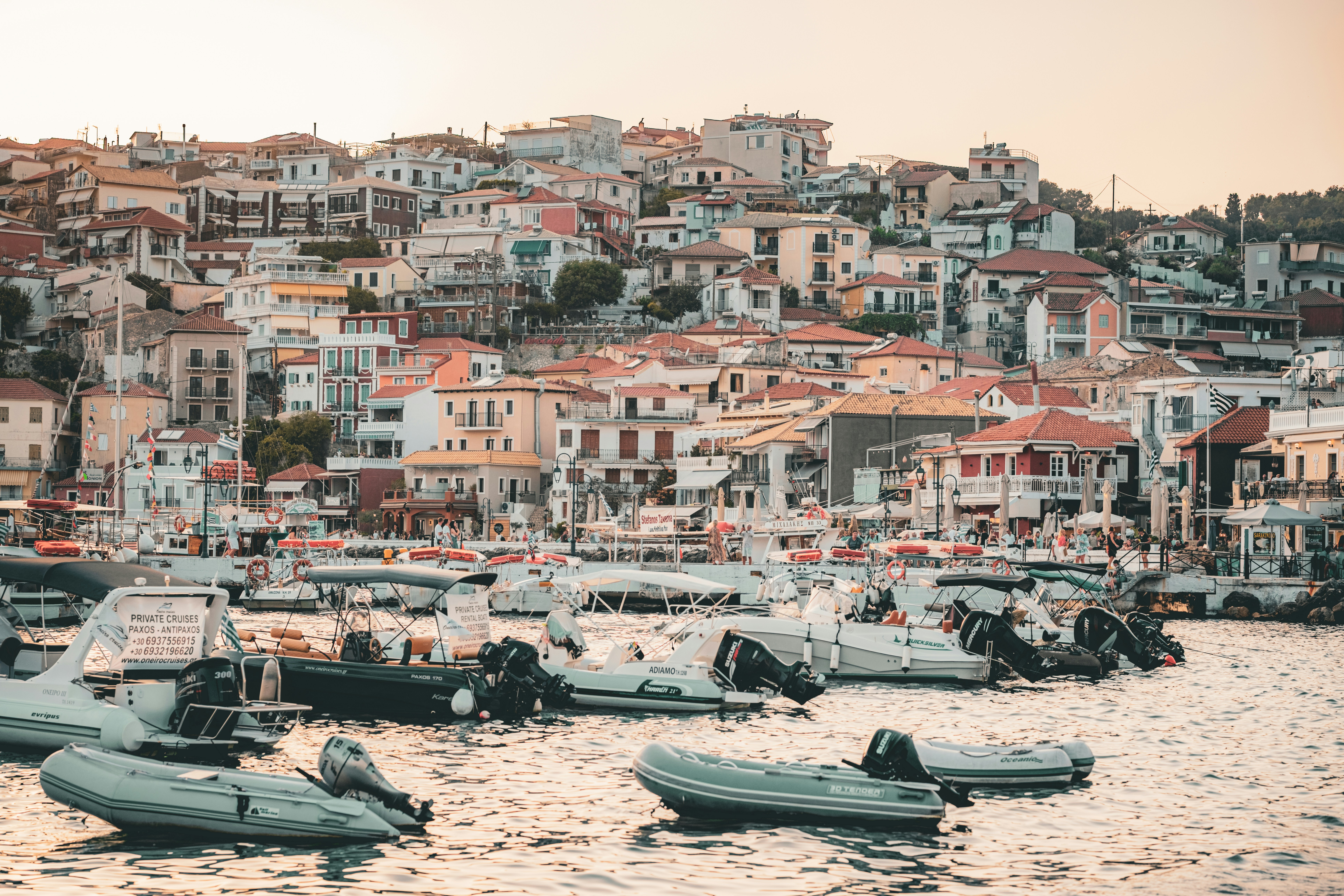 Small motorboats moored at a harbor below a hillside town with terracotta roofs