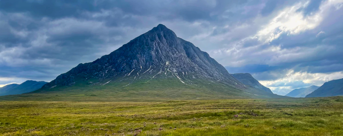 Buachaille Etive Mor rising to a sharp peak above flat green moorland under a heavy grey sky