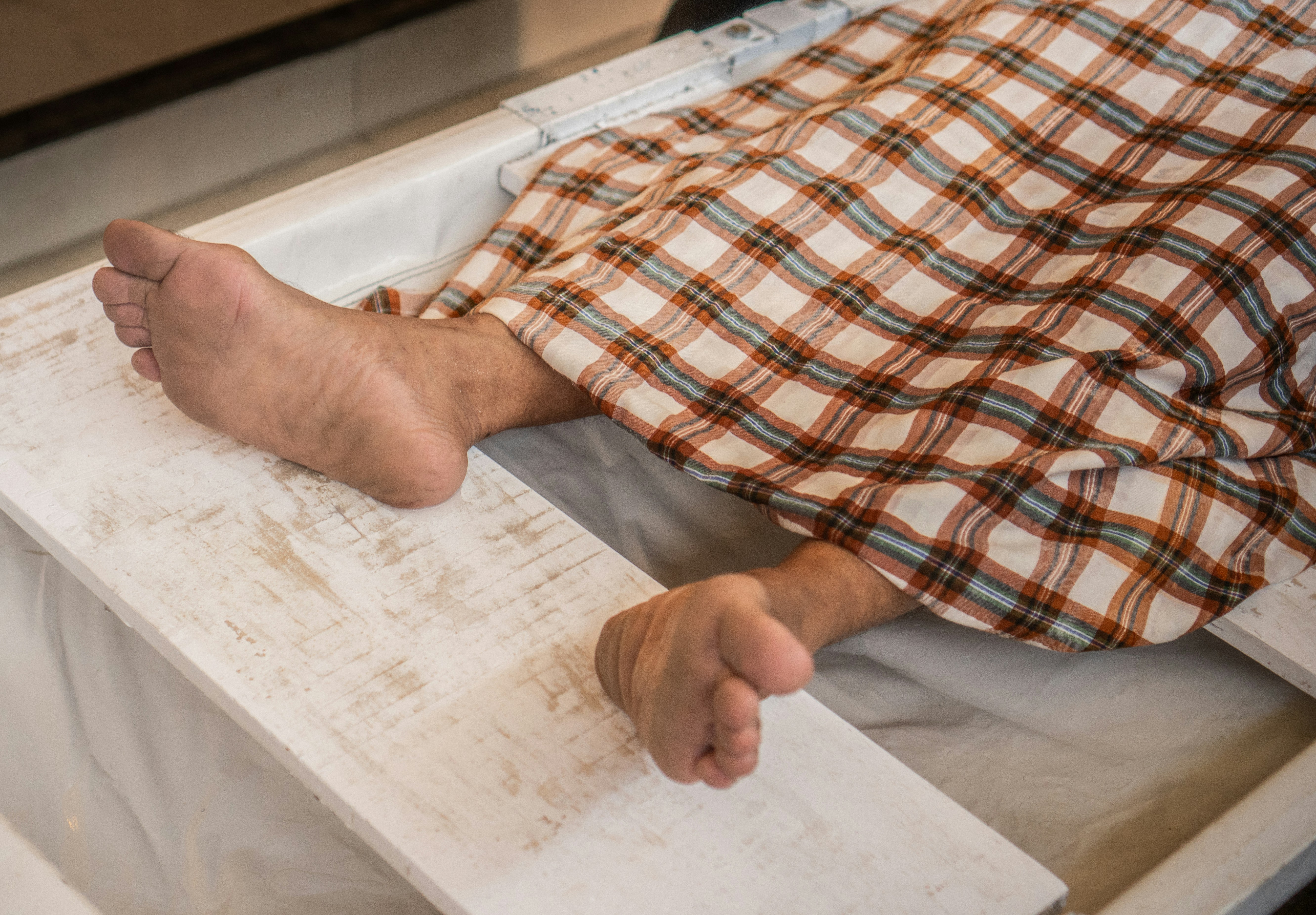 Piedi nudi di una persona appoggiata su una tavola di legno bianco sotto una coperta a quadri