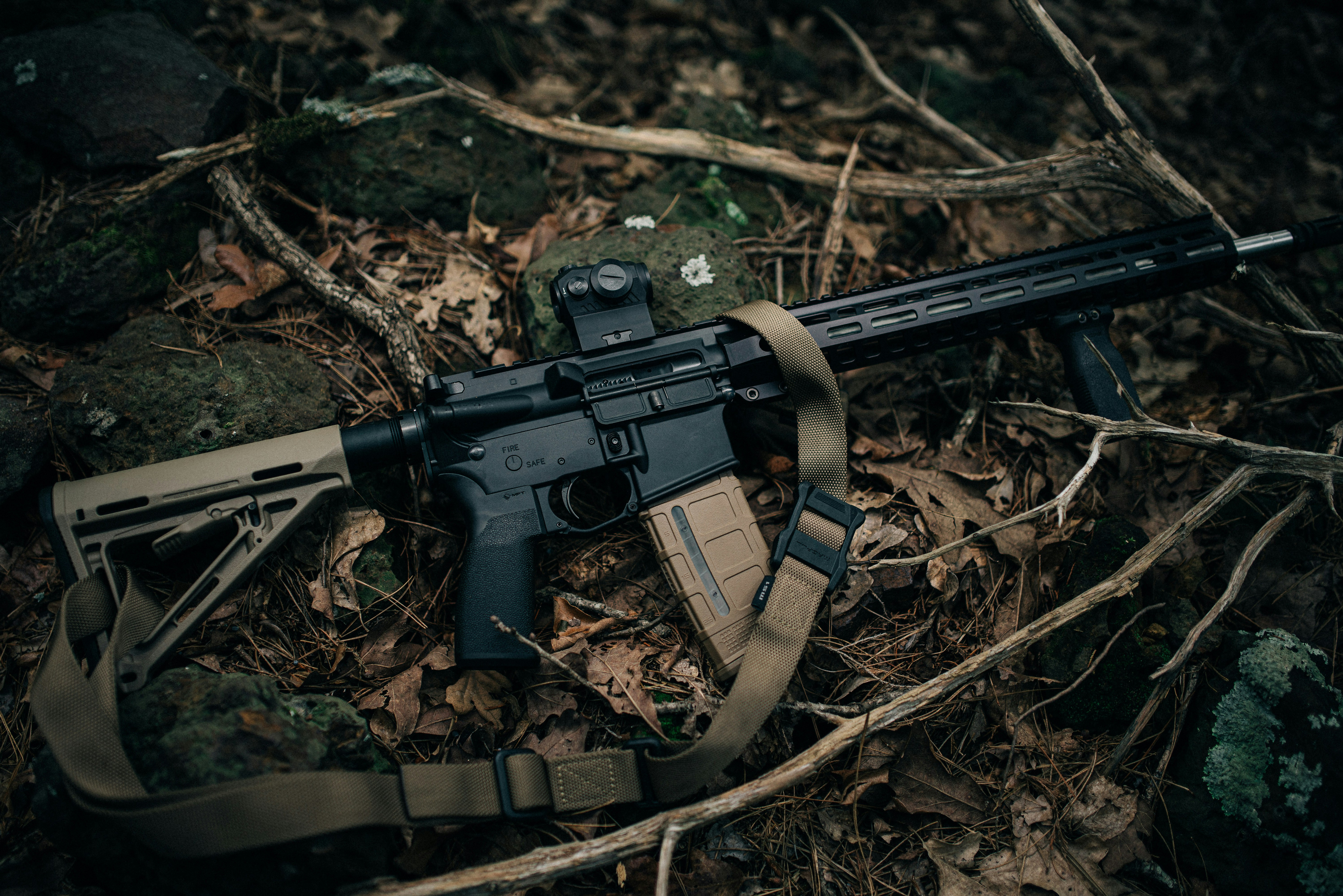 Um rifle preto com coronha bege e carregador no chão da floresta