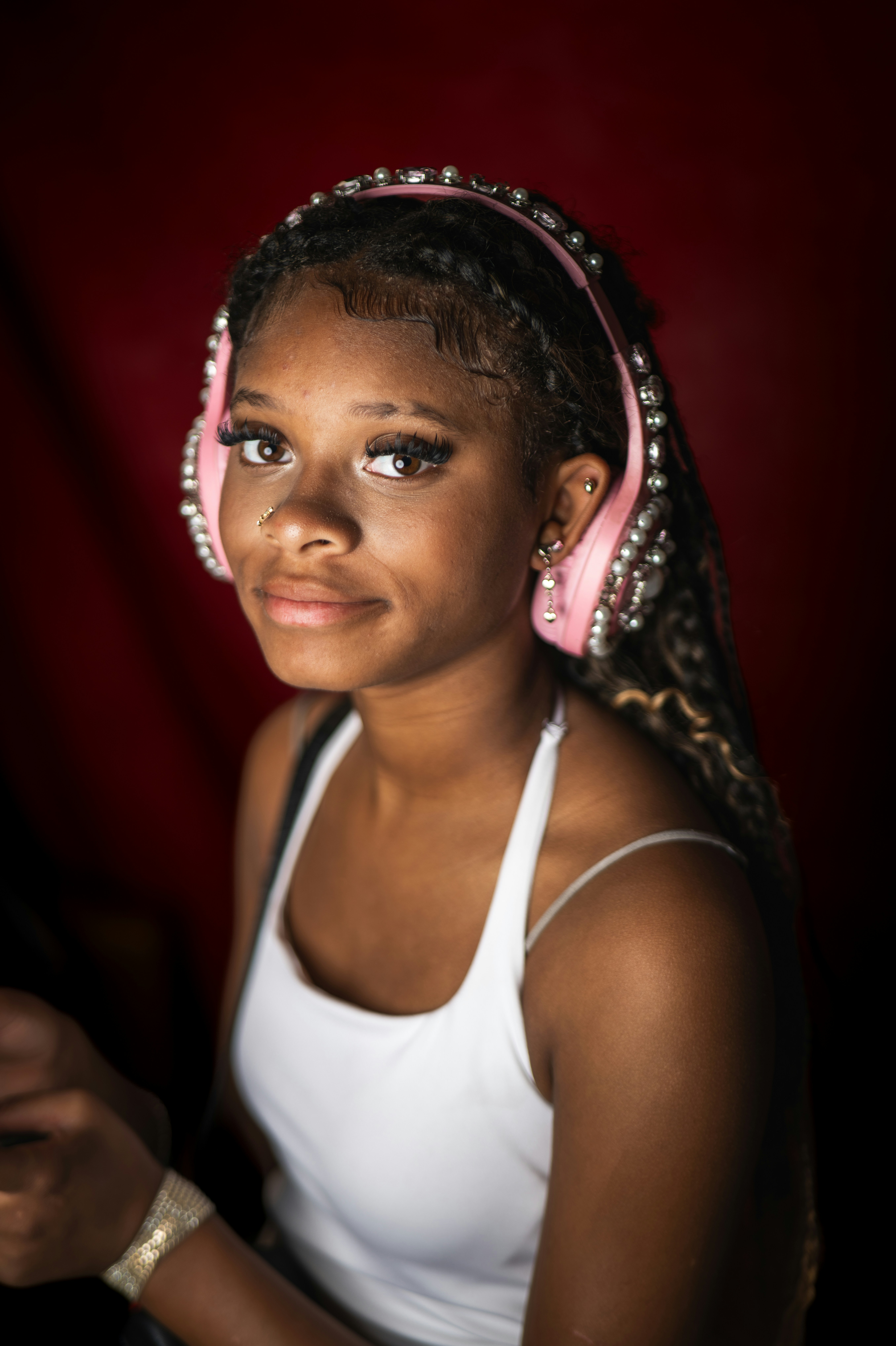 A young woman wearing pink headphones decorated with pearls against a dark red background