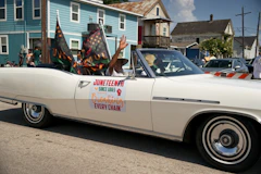A man waving from a white convertible carrying a Juneteenth sign during a street parade