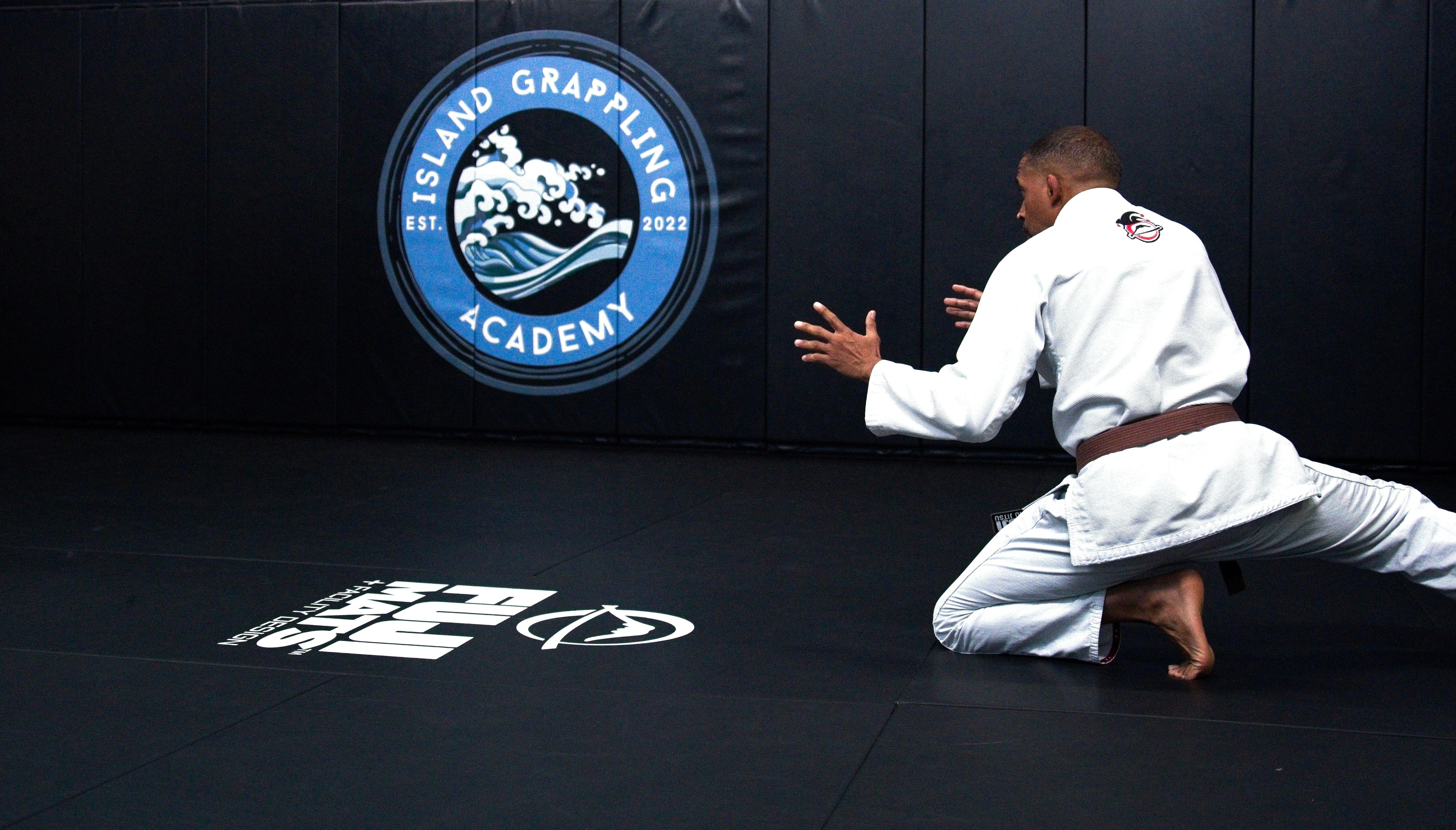 A person in a white gi kneeling on a black mat in a gym