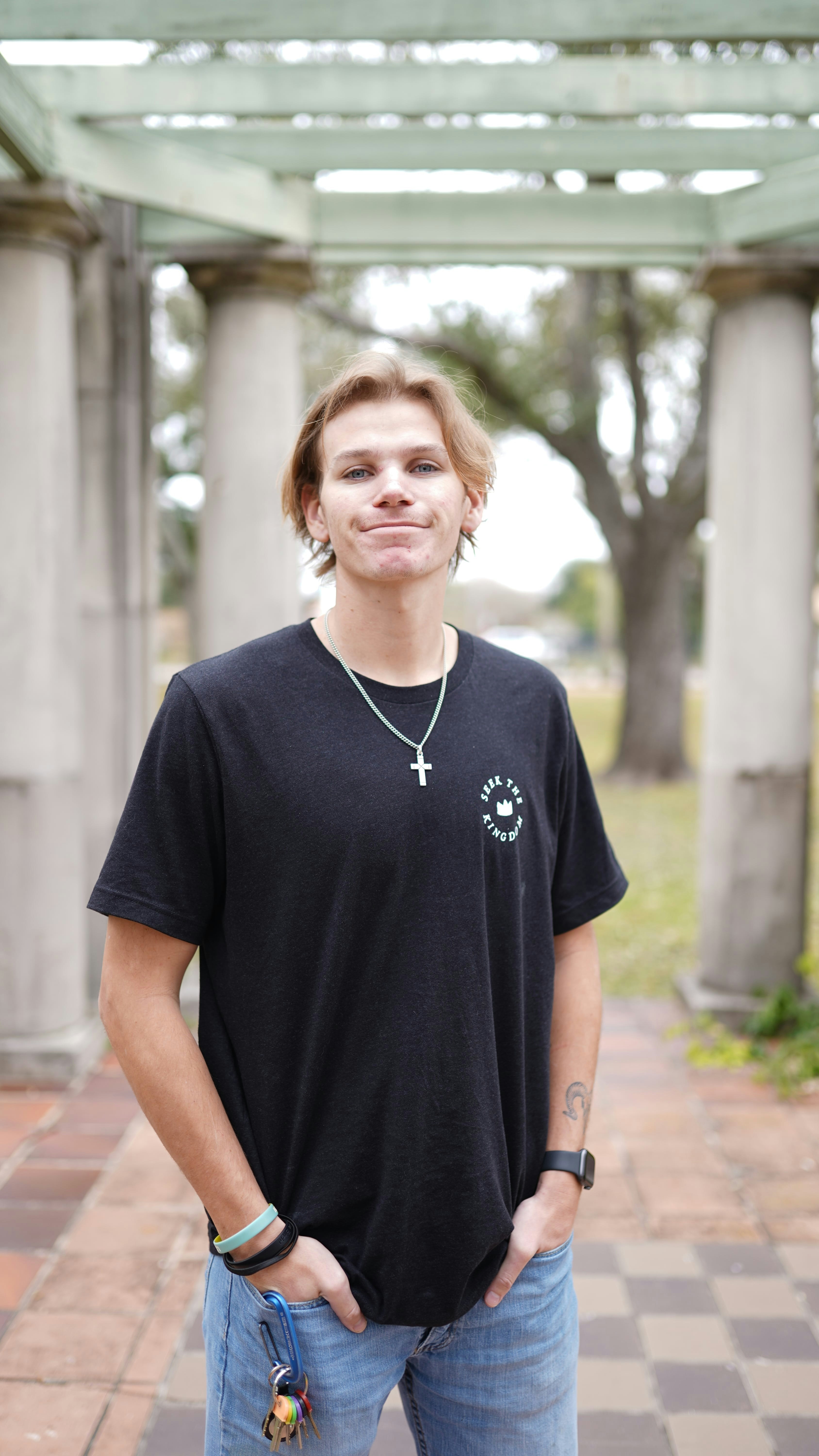 A young man in a black t-shirt and jeans with a cross necklace