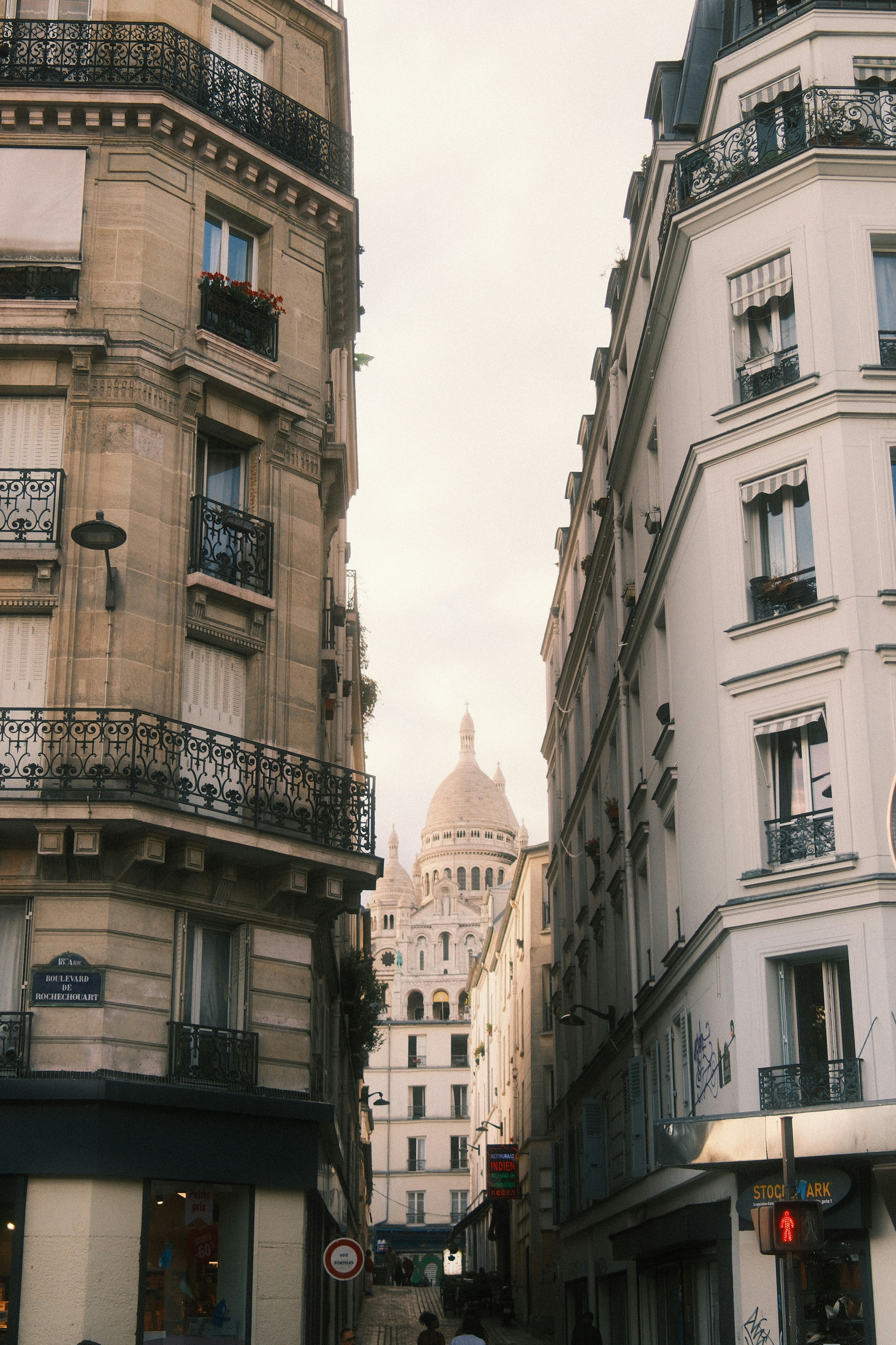 The Sacré-Cœur basilica visible between two classic Parisian apartment buildings on a street