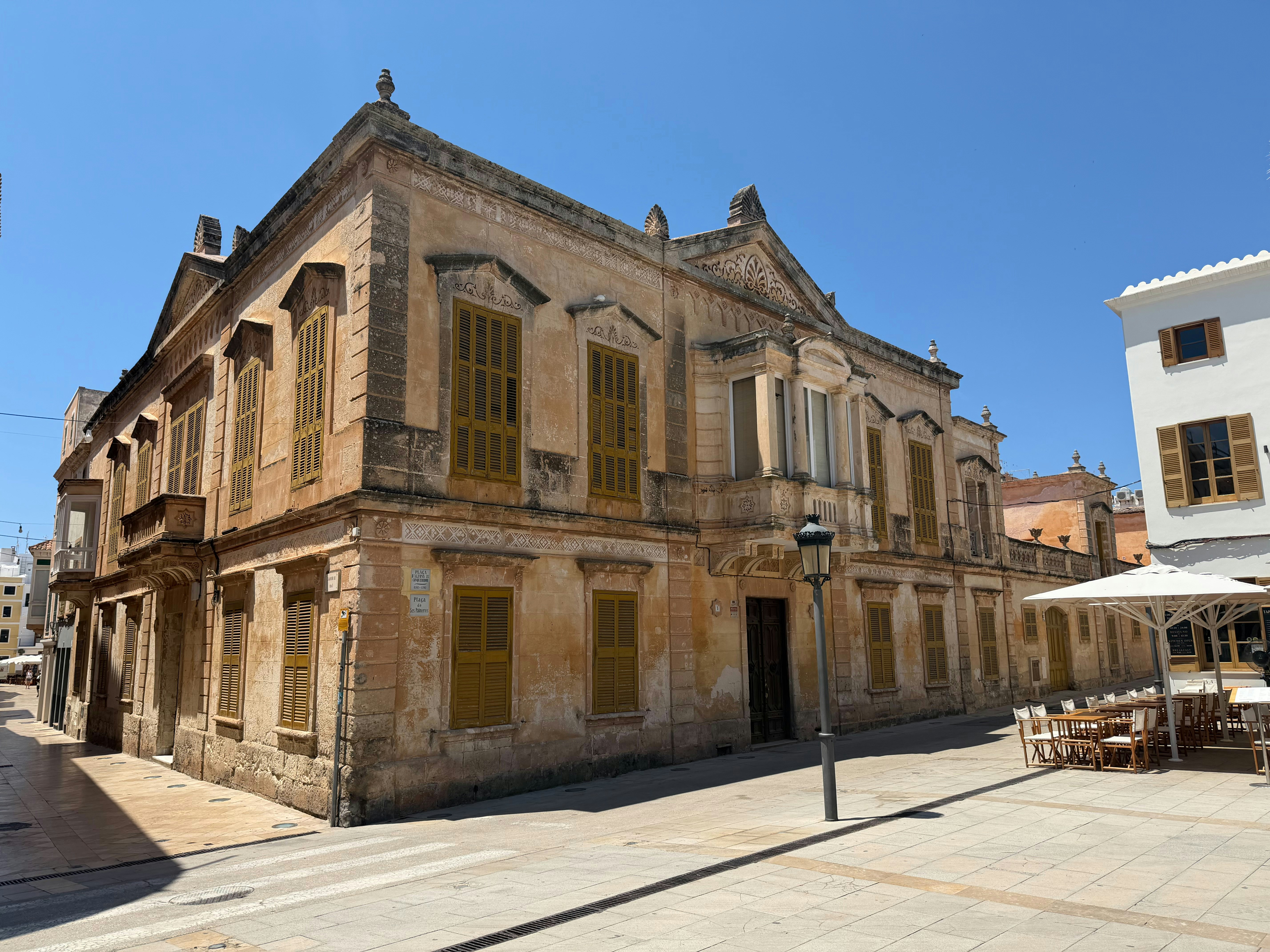 A historic stone building with yellow shutters on a sunny street in Ciutadella