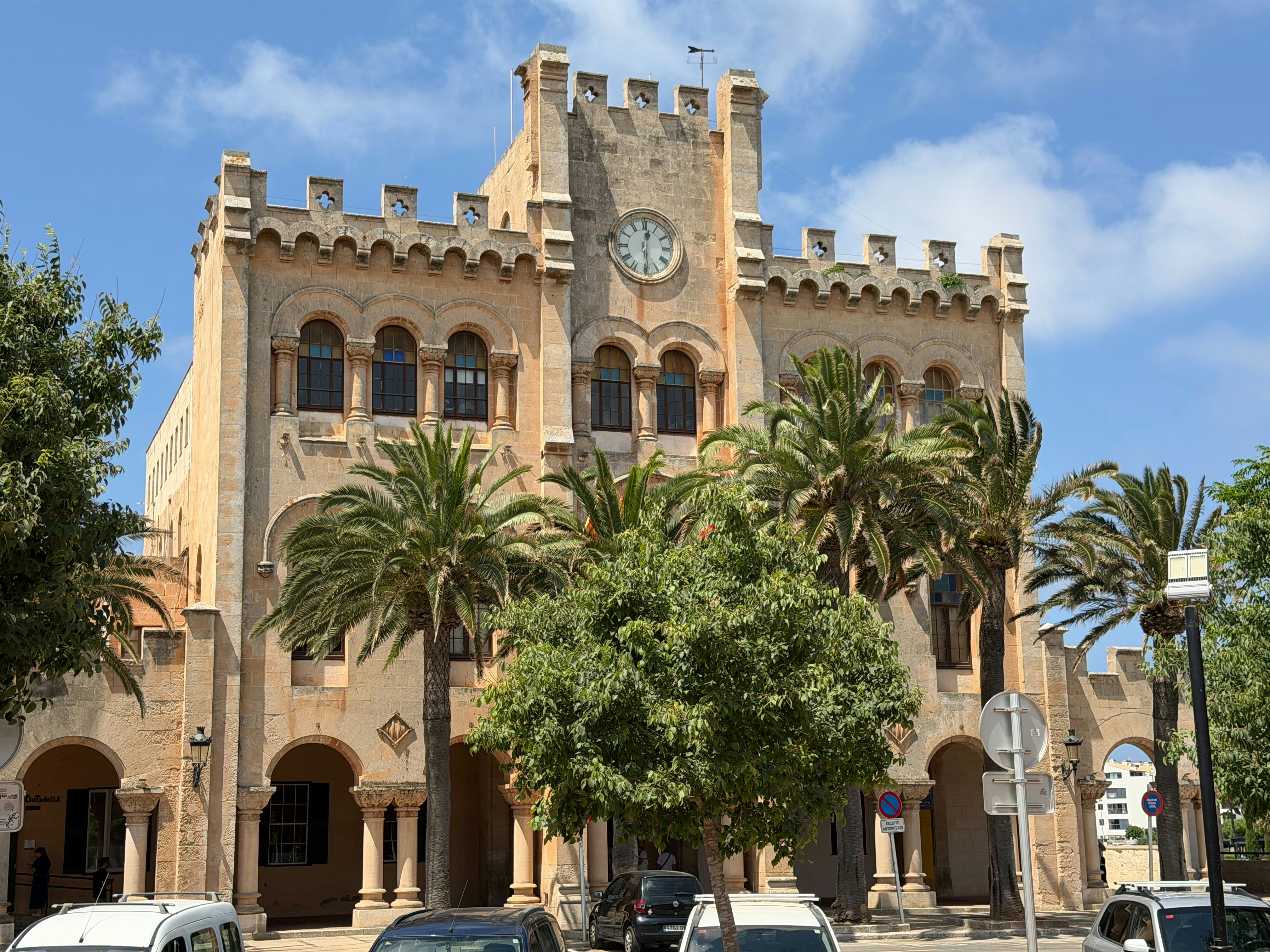 The historic town hall building with a clock tower and palm trees in Ciutadella