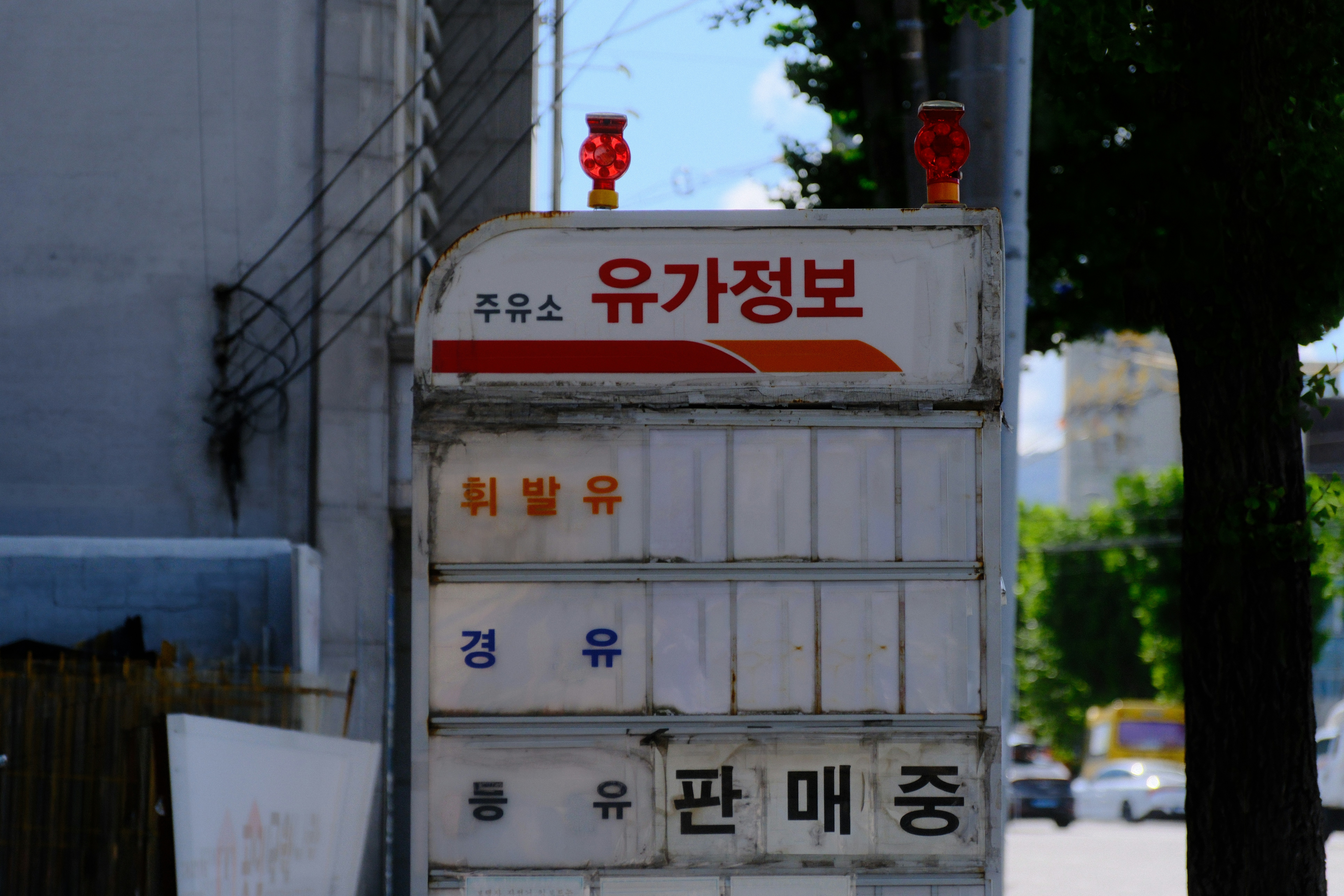 A weathered gas station price sign with Korean text on a city street