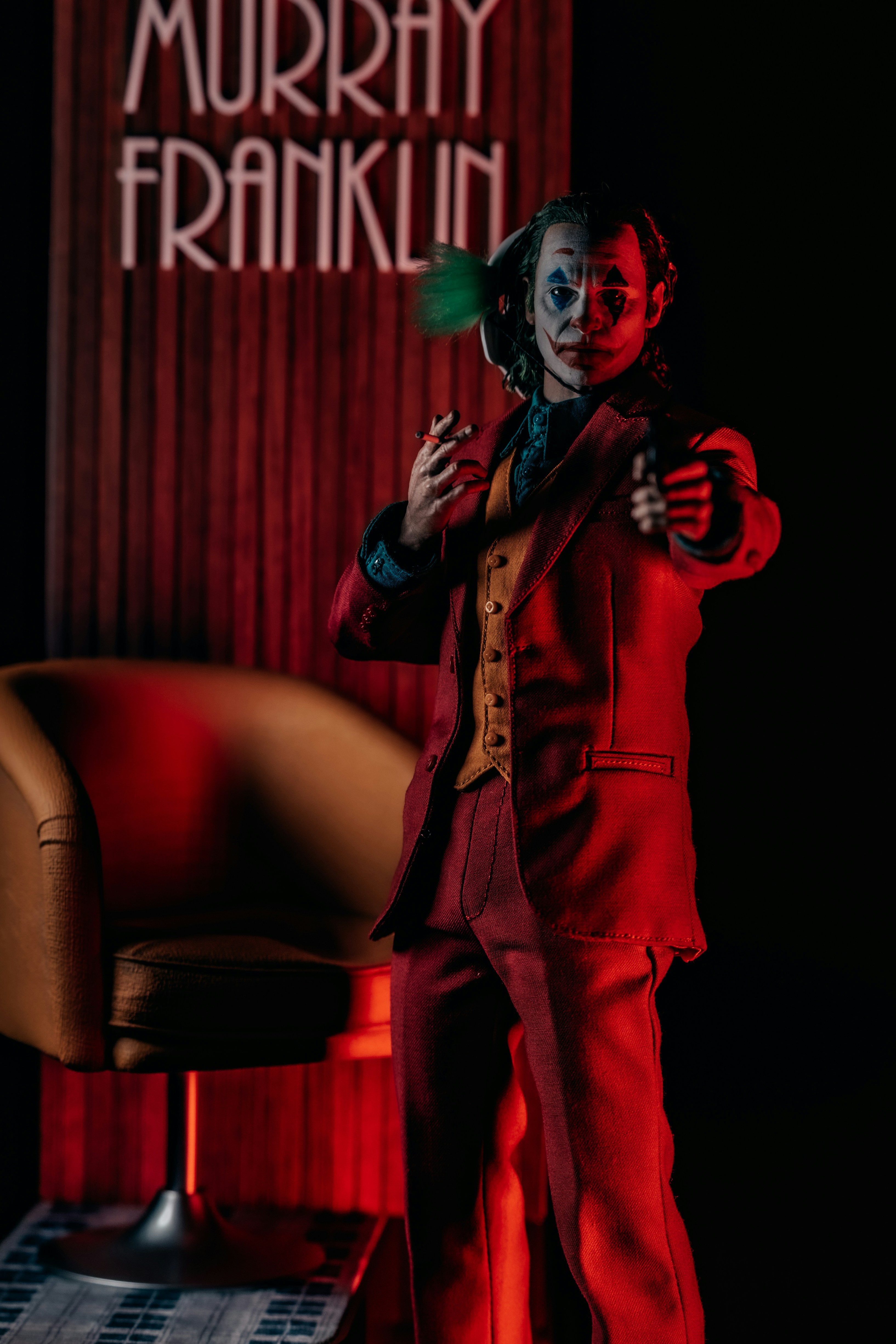 A person in clown makeup and a red suit pointing a handgun