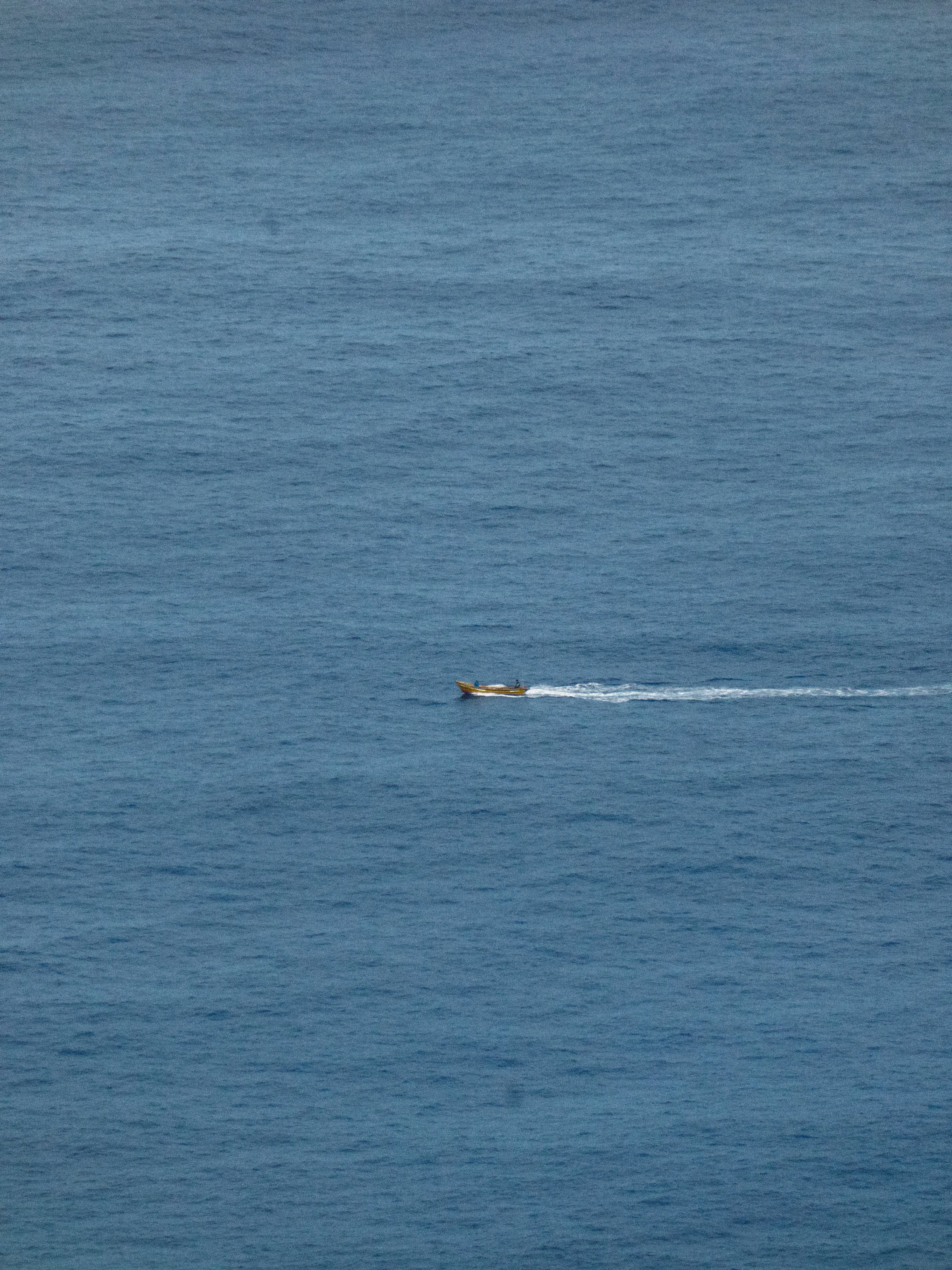 A small yellow boat moving across the vast blue ocean