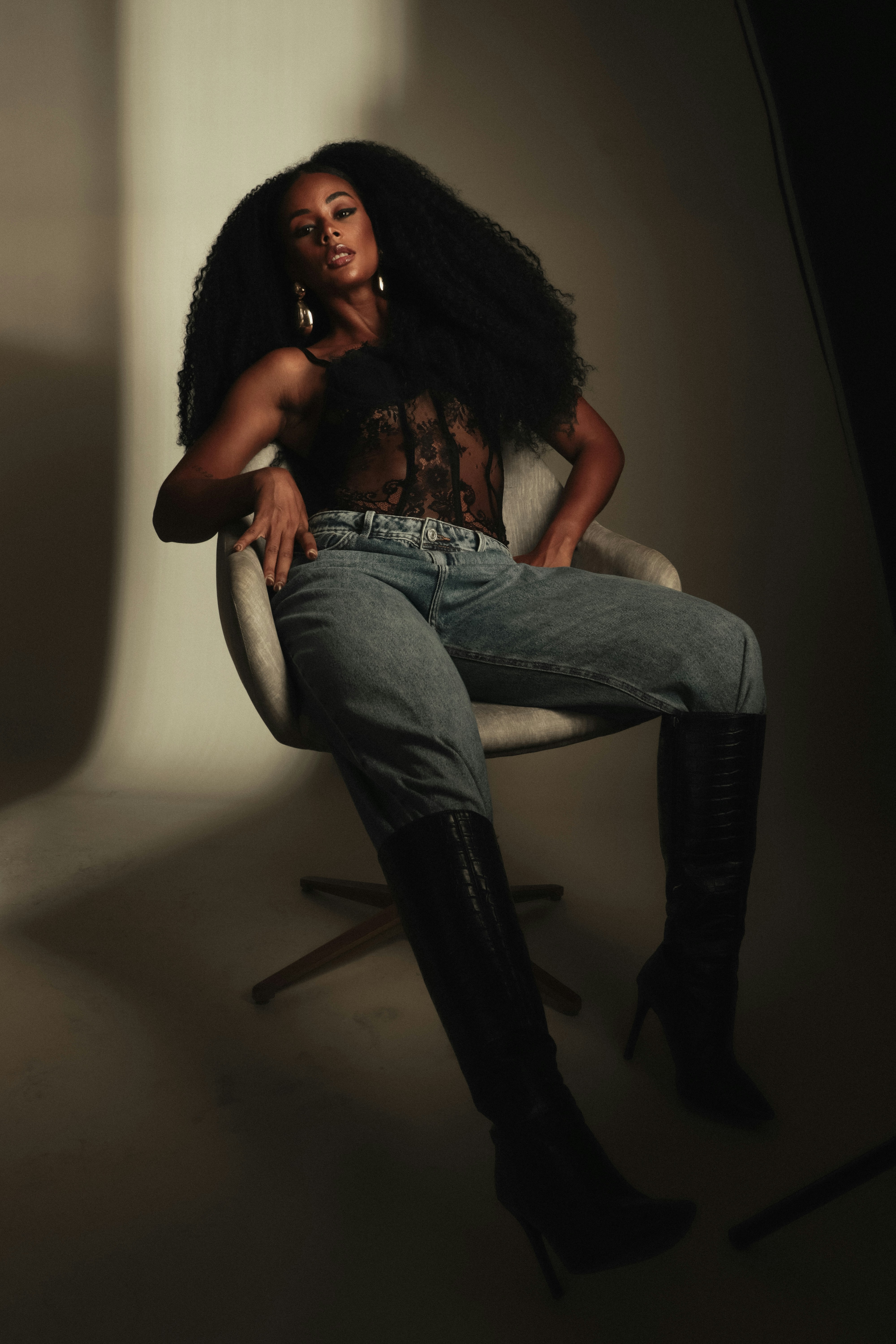 A woman with long curly hair in a black lace top and jeans