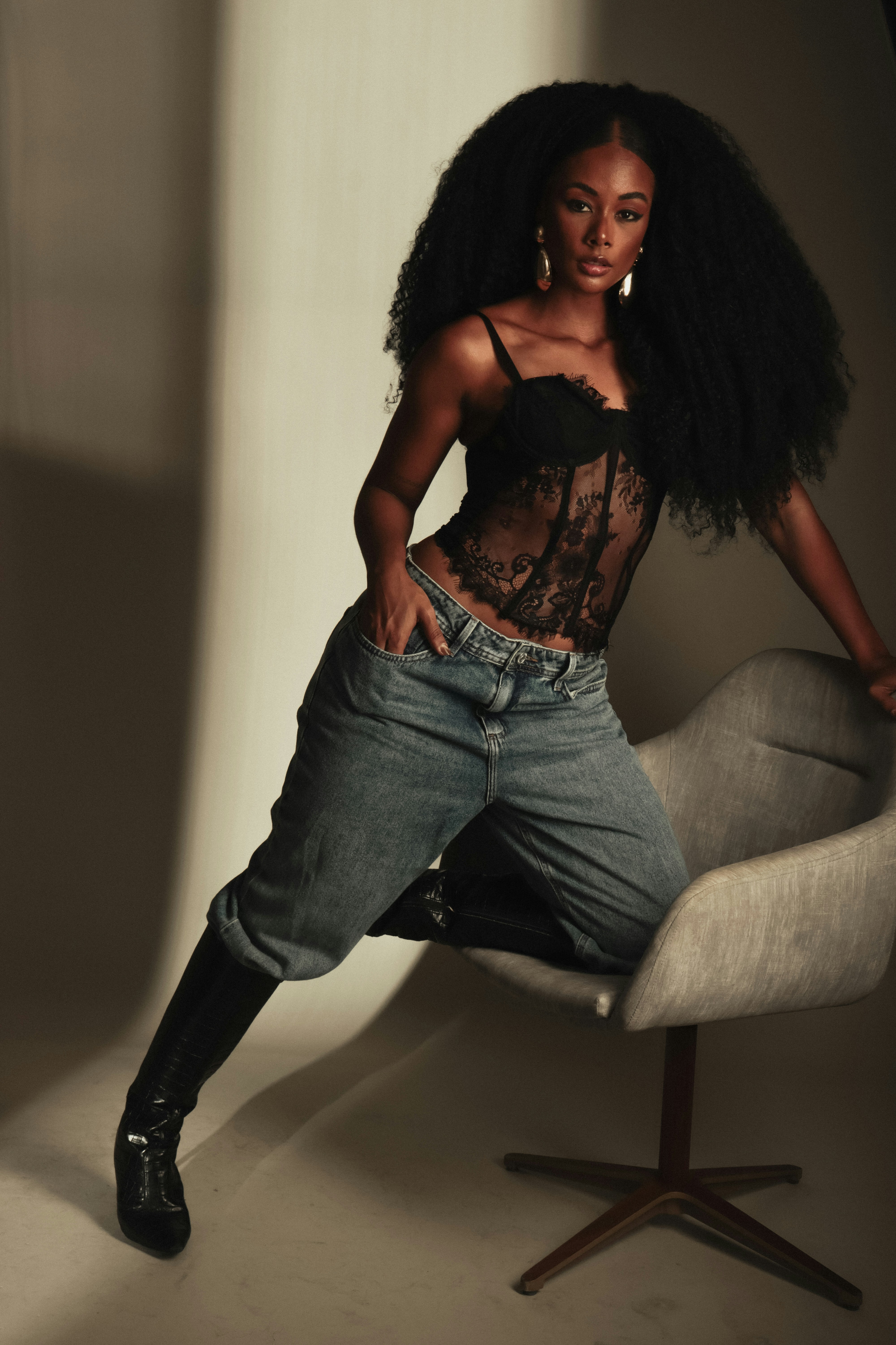 A woman with long curly hair wearing a black lace corset and blue jeans