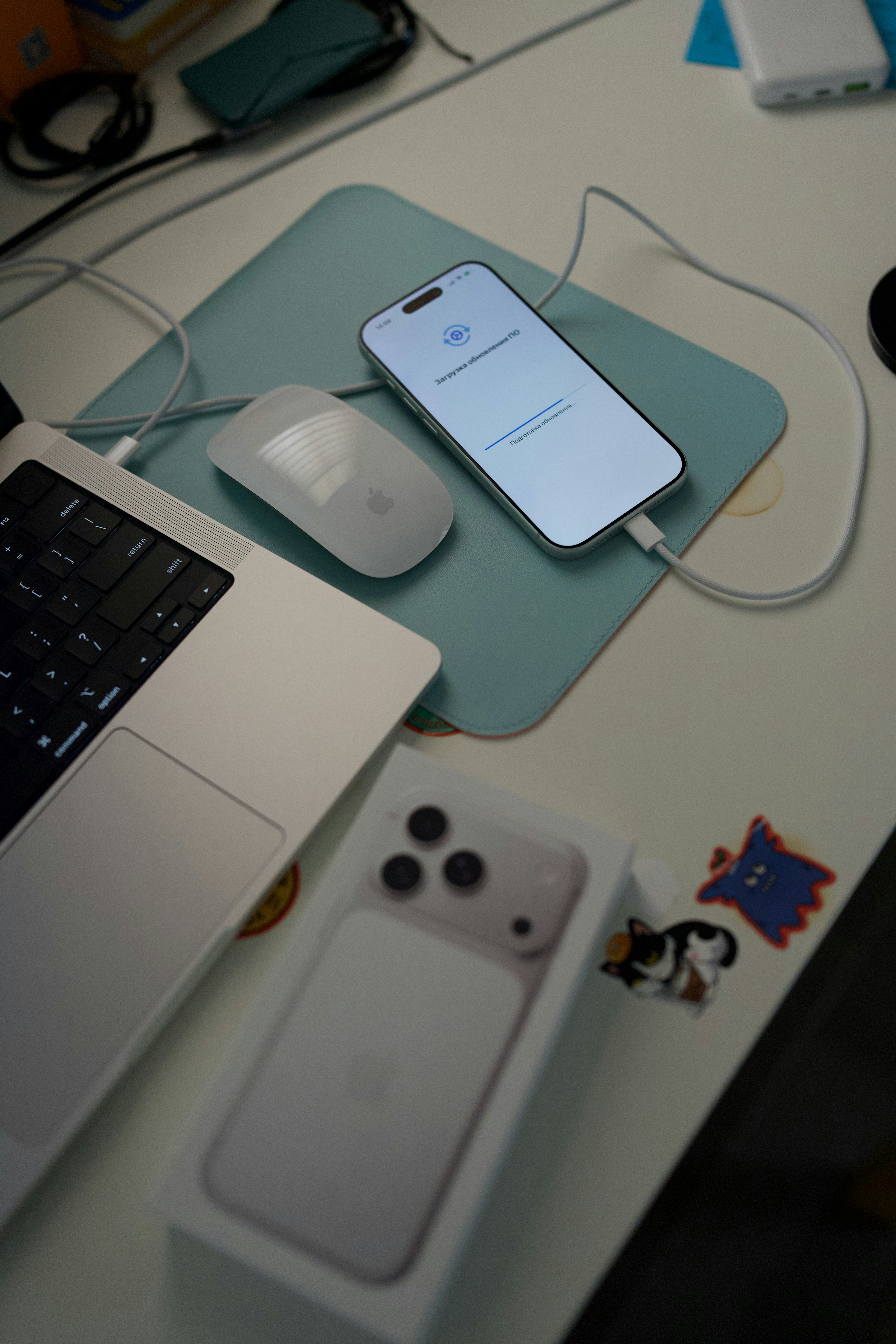 Close-up of an Apple Magic Mouse, iPhone charging, and MacBook keyboard on a minimalist desk pad.