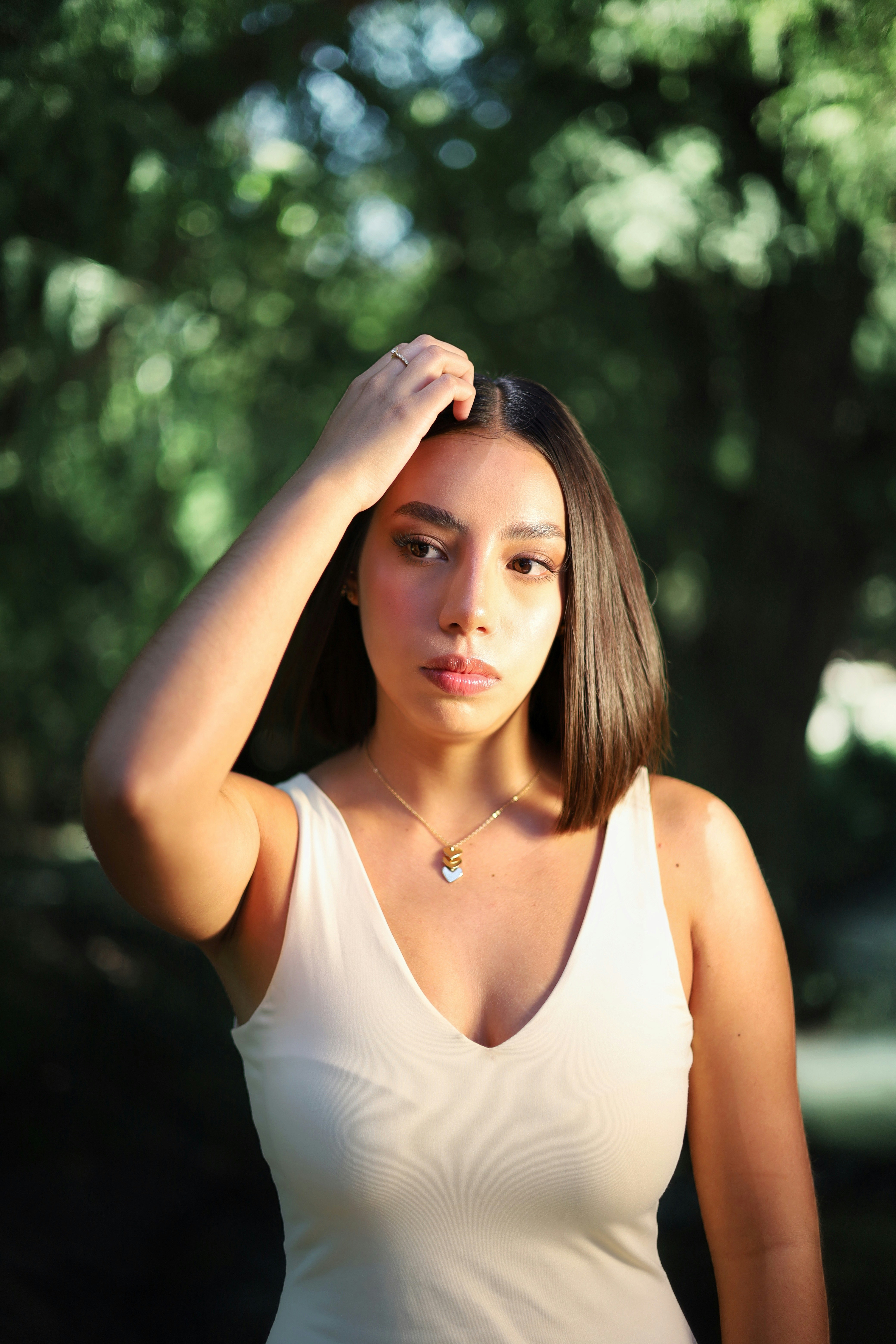 A woman with a bob haircut touching her hair in a sunlit park