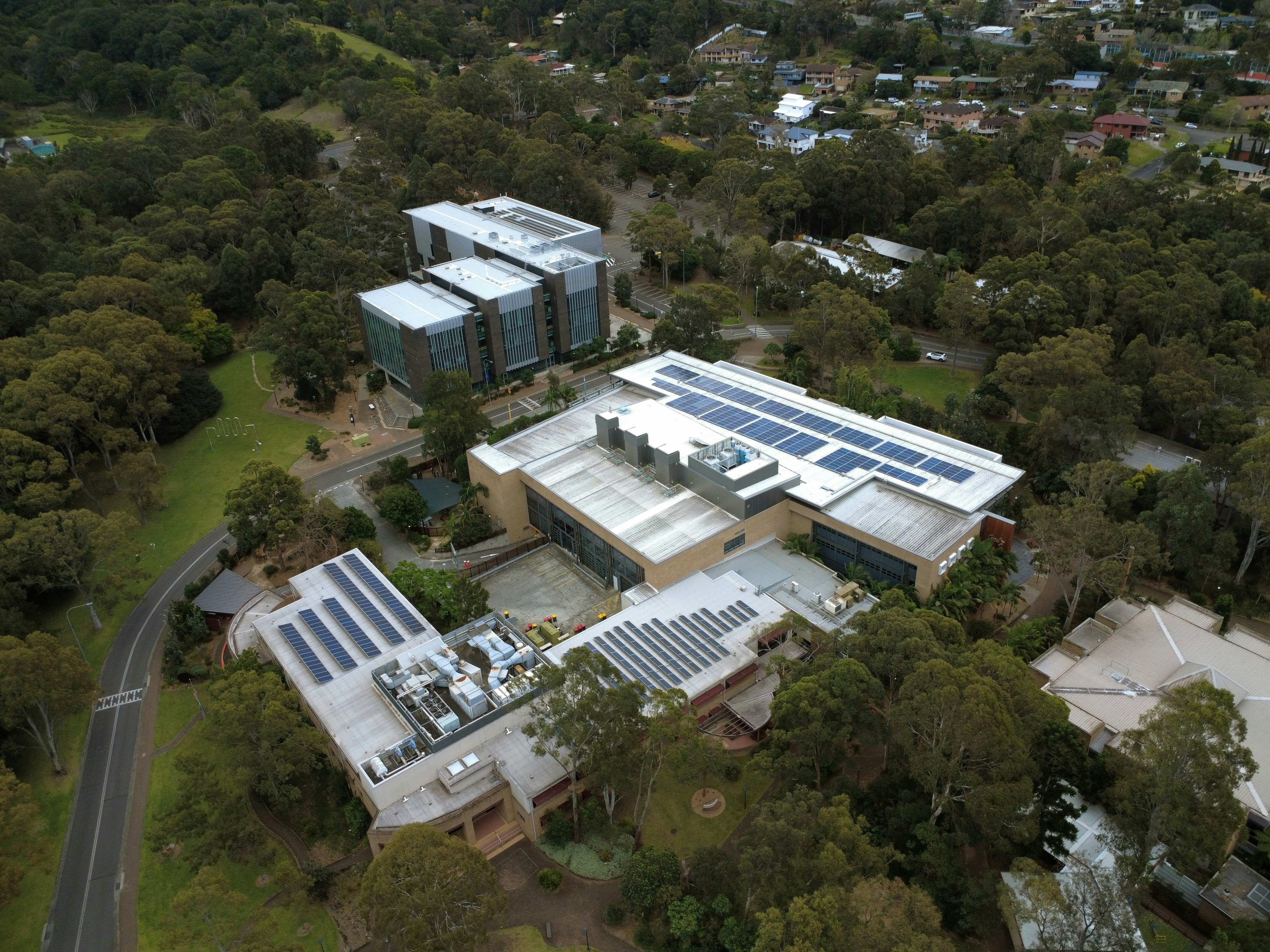 Vista aérea de edifícios modernos com painéis solares cercados por uma densa floresta verde