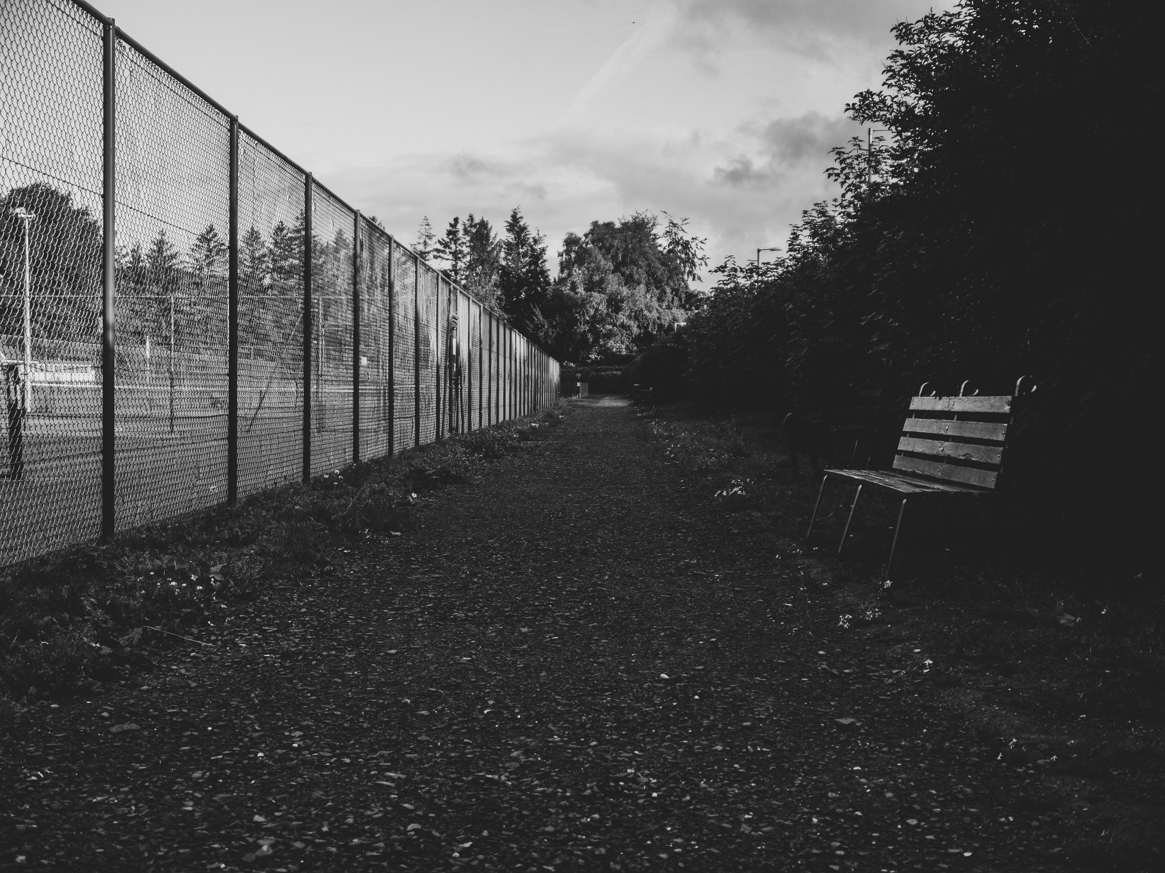 A wooden bench beside a gravel path and a tall chain-link fence