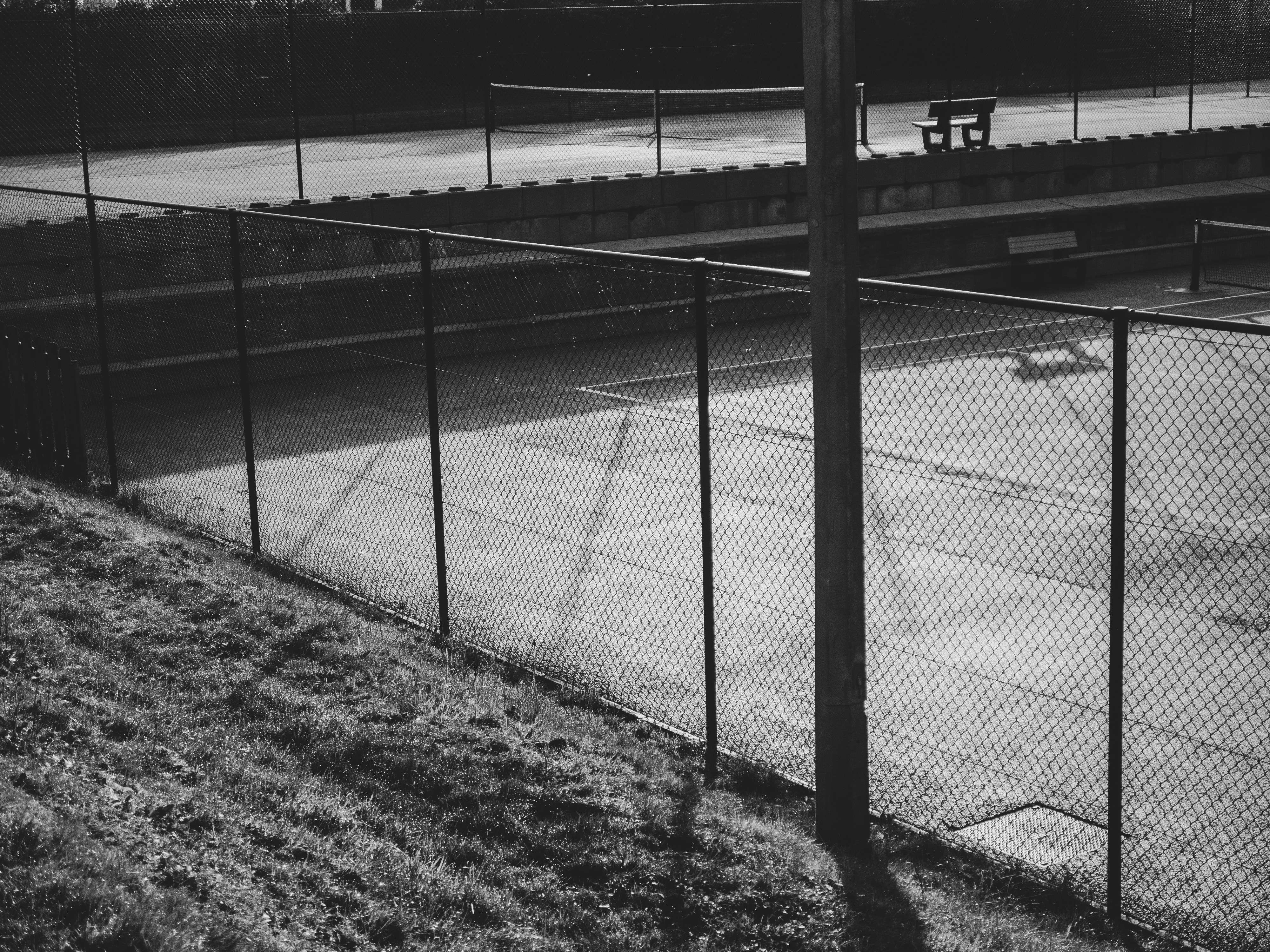 A chain link fence bordering a tennis court with a bench in the background