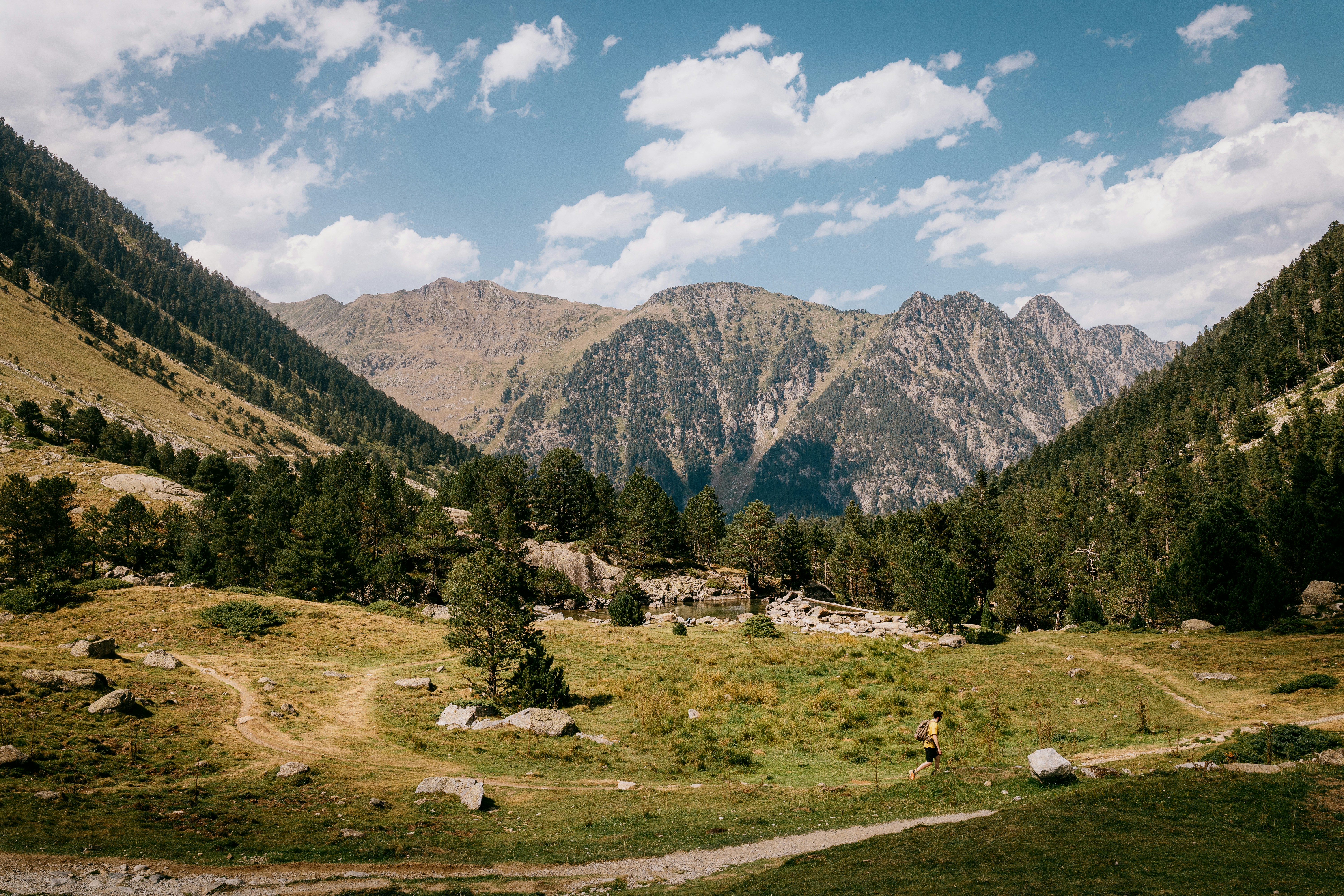 A person with a backpack walking on a dirt path through a mountain valley