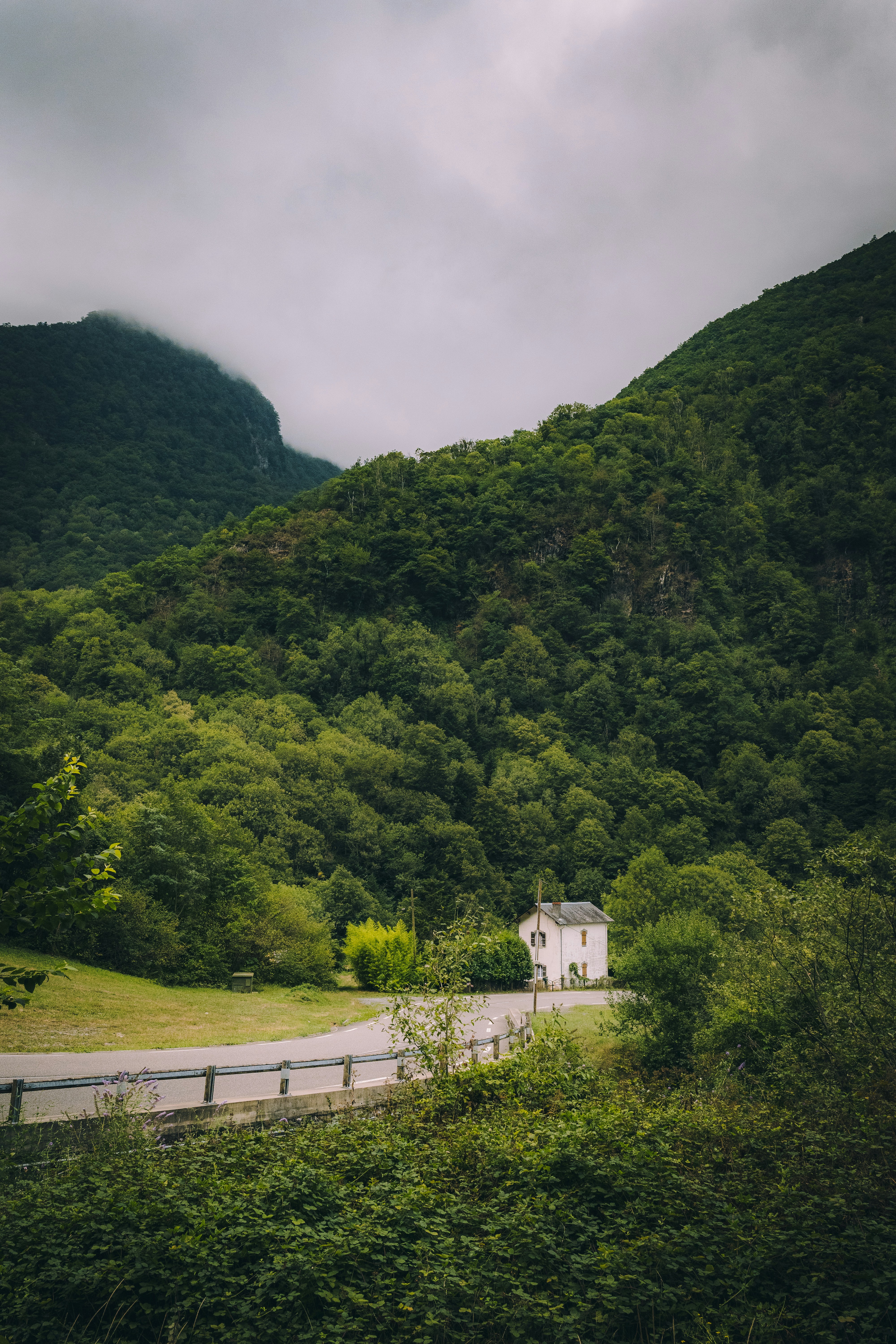 A small white house beside a winding road in a lush green mountain valley