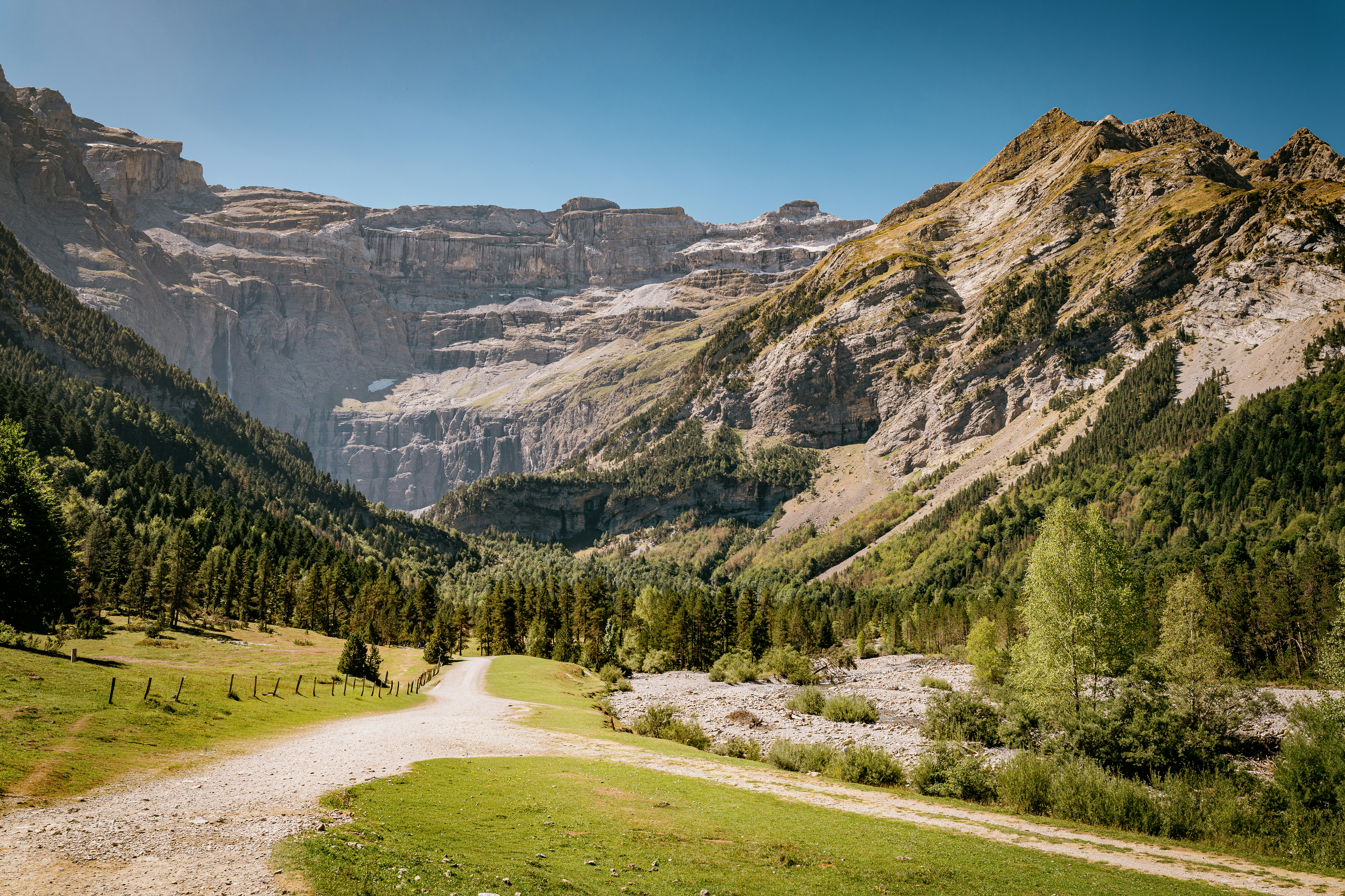 A dirt path leading toward a massive rocky mountain cirque under a clear sky