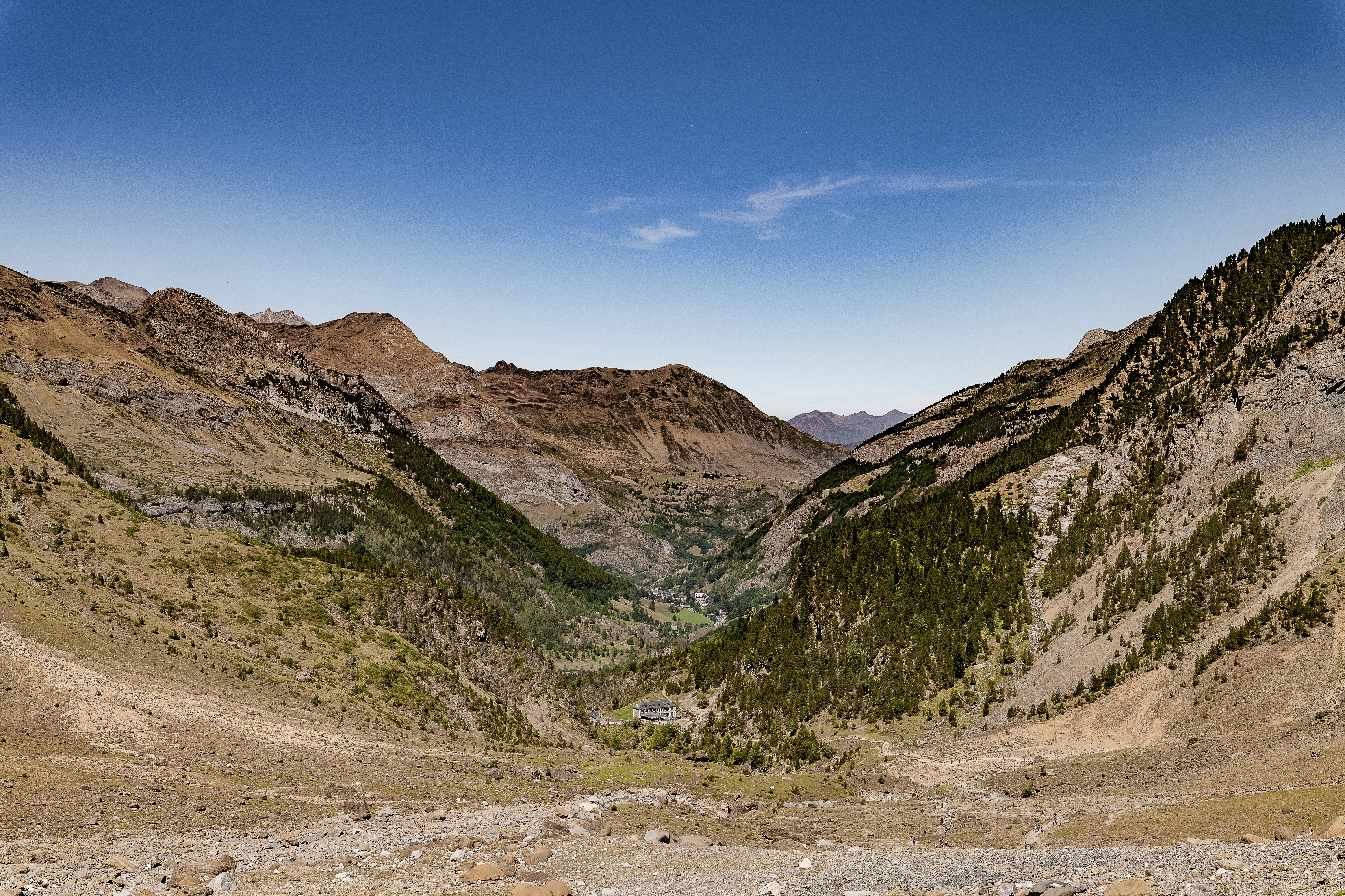 A deep mountain valley with pine forests and rocky slopes under a clear sky