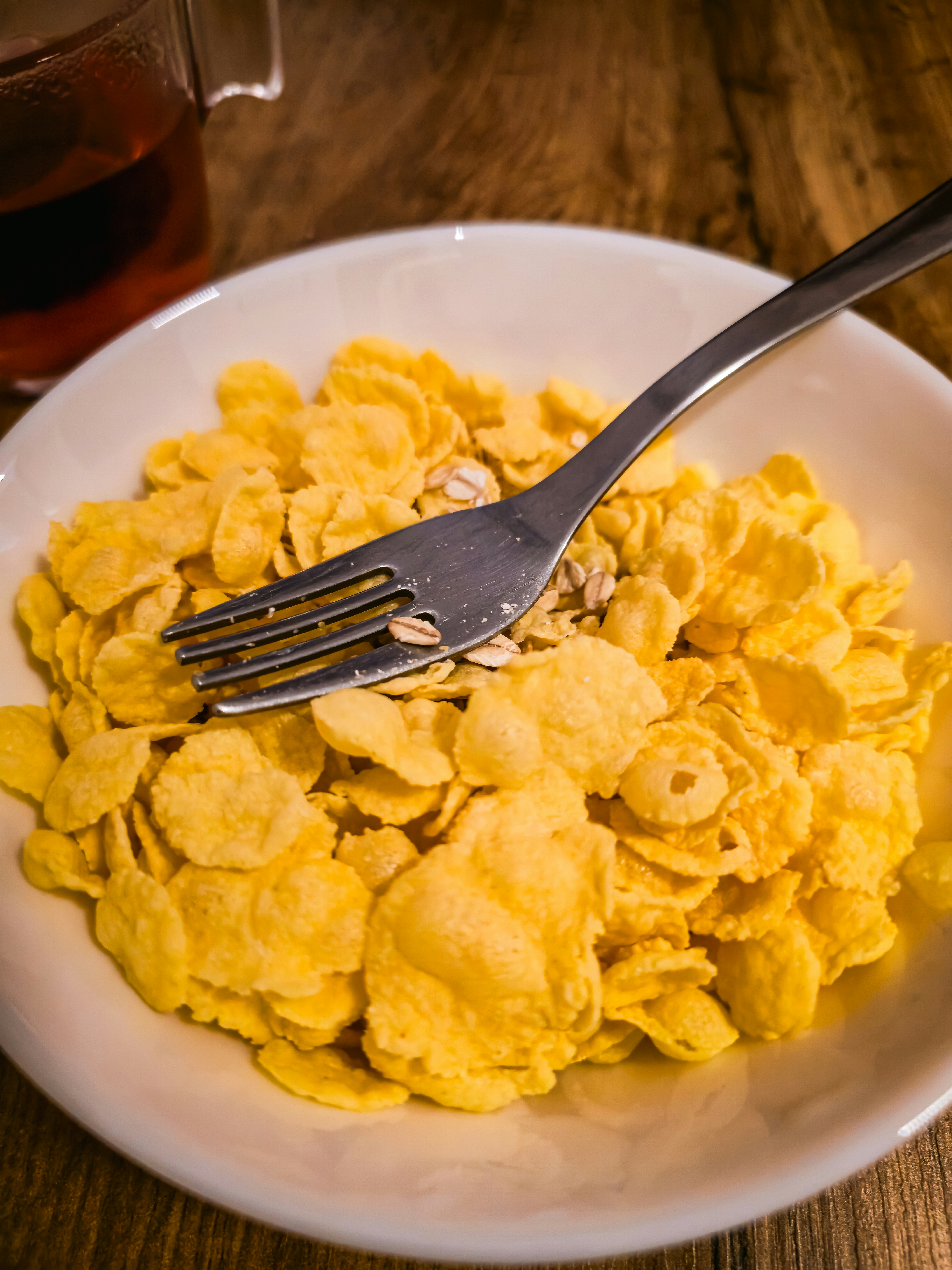 Une fourchette en métal reposant dans un bol blanc de cornflakes jaunes sur du bois