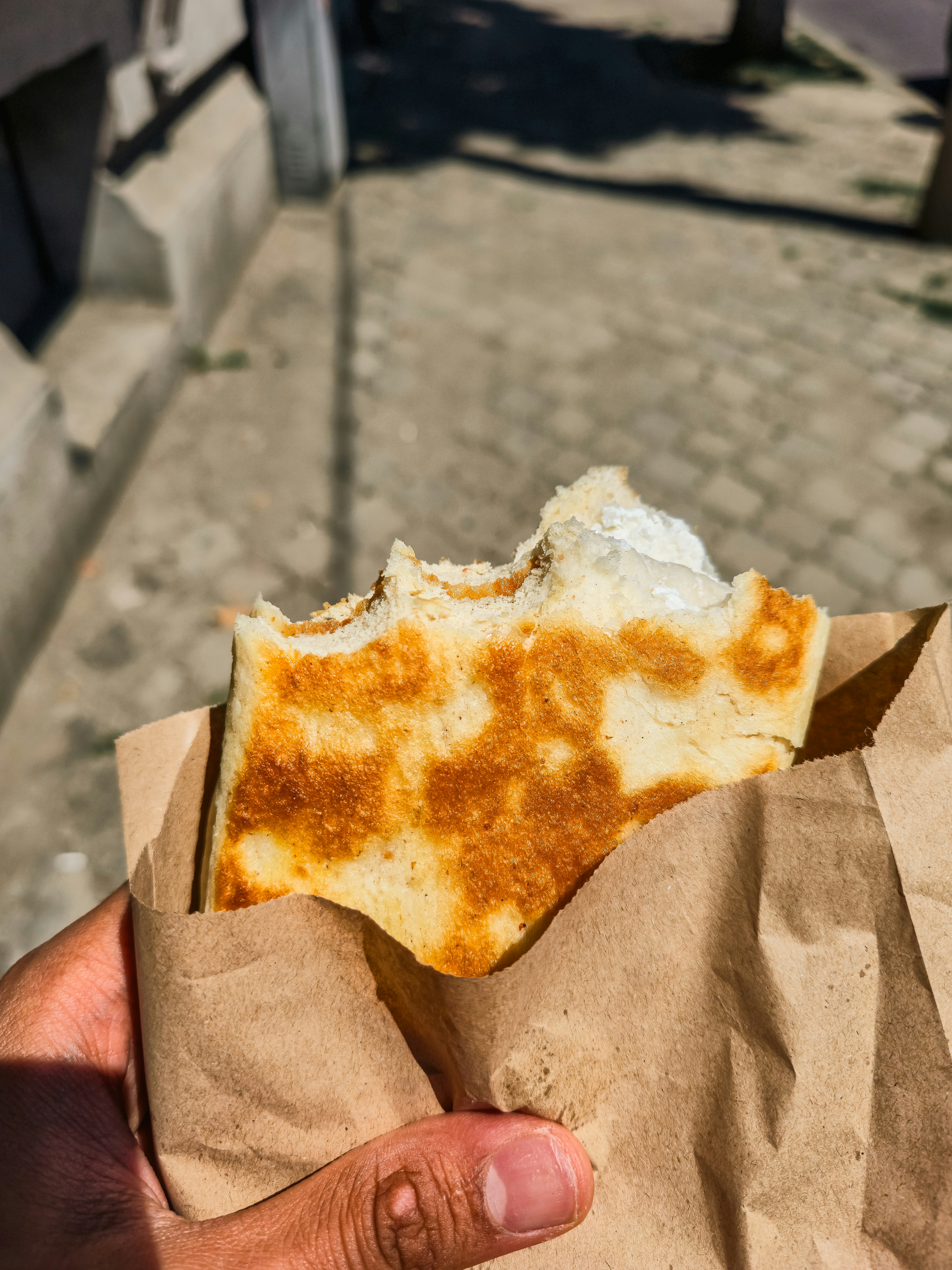 A hand holding a partially eaten flatbread in a brown paper bag outdoors