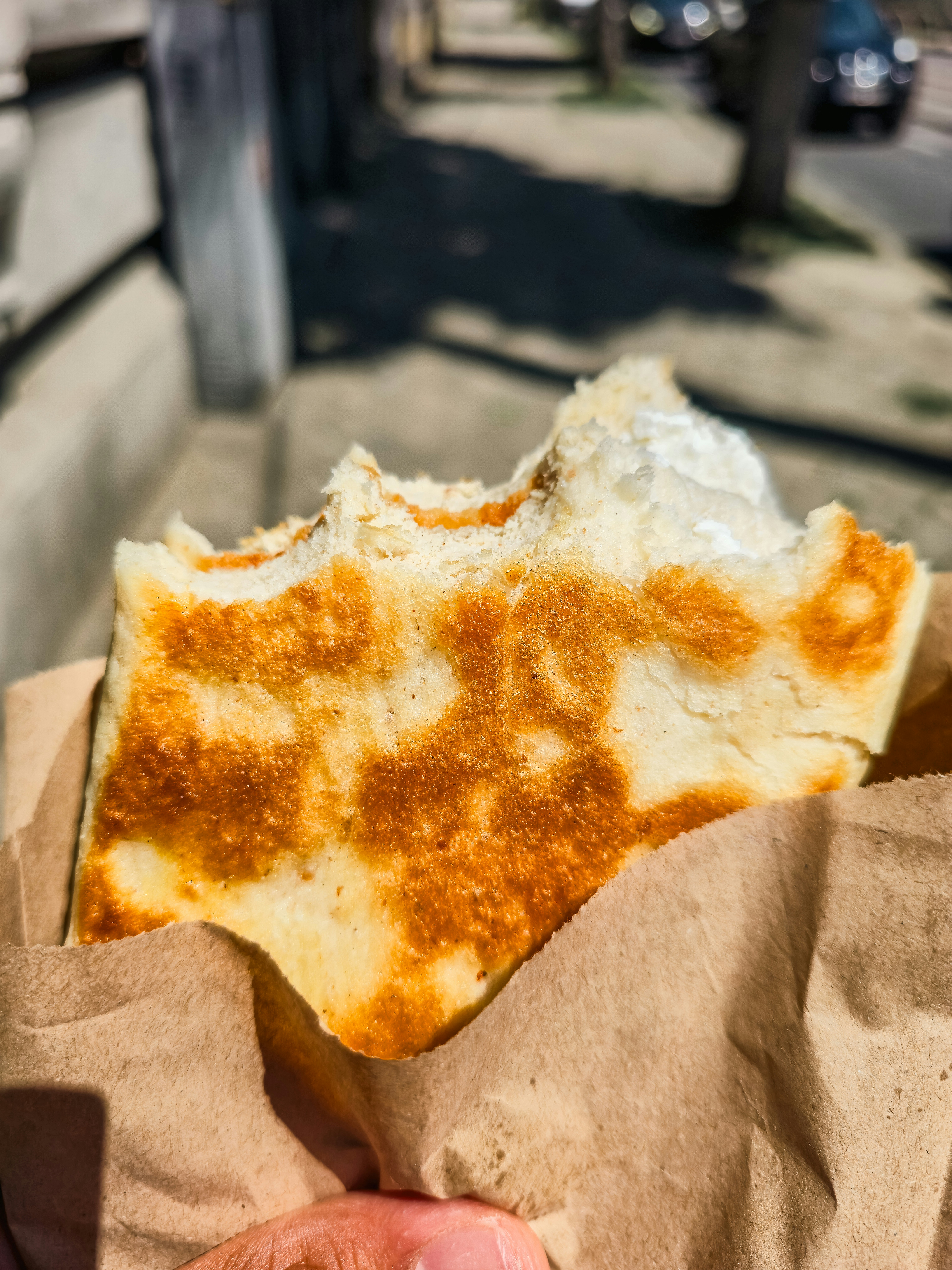 A partially eaten flatbread in a brown paper bag held outdoors