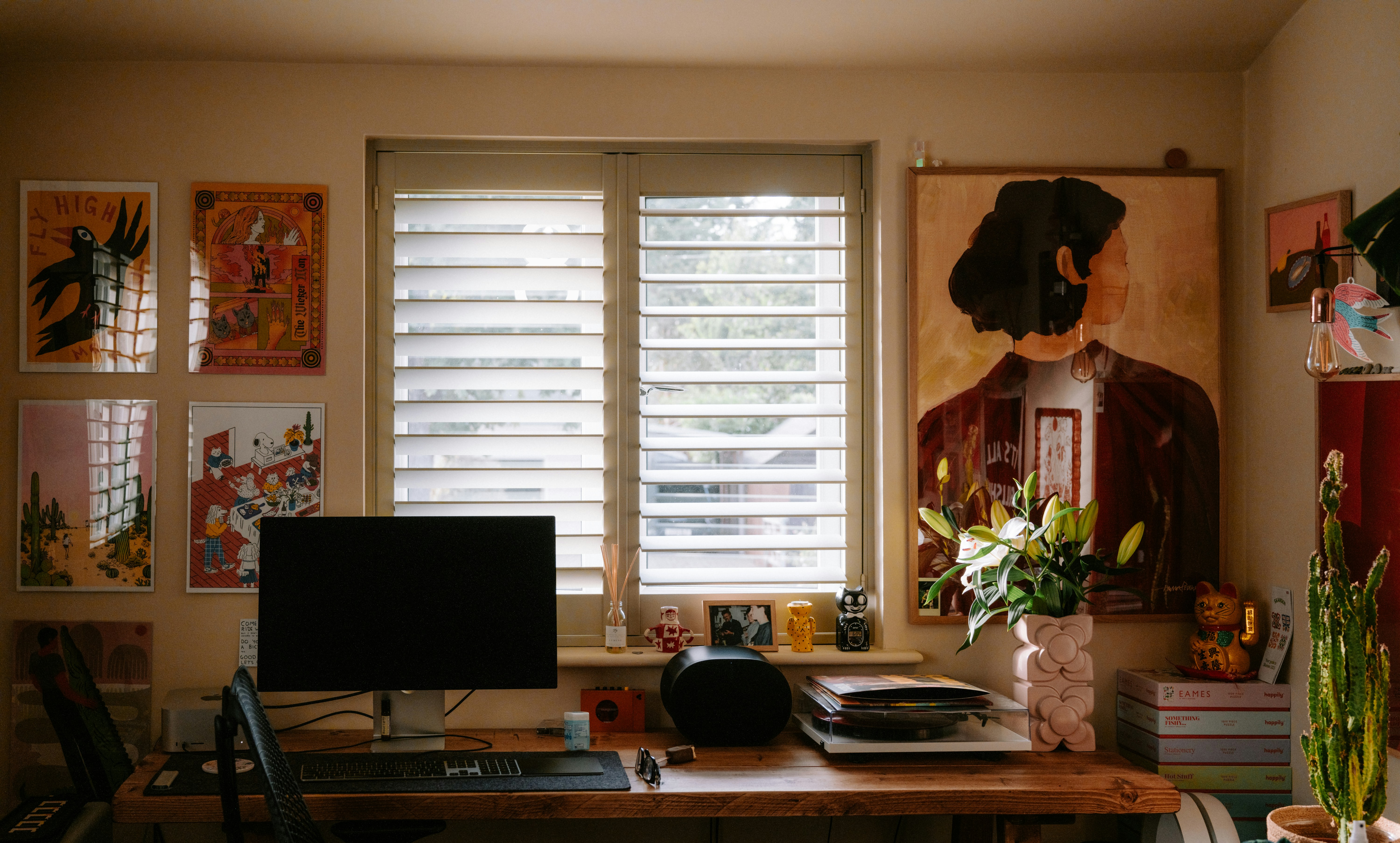 A home office desk with a computer monitor, flowers, and wall art