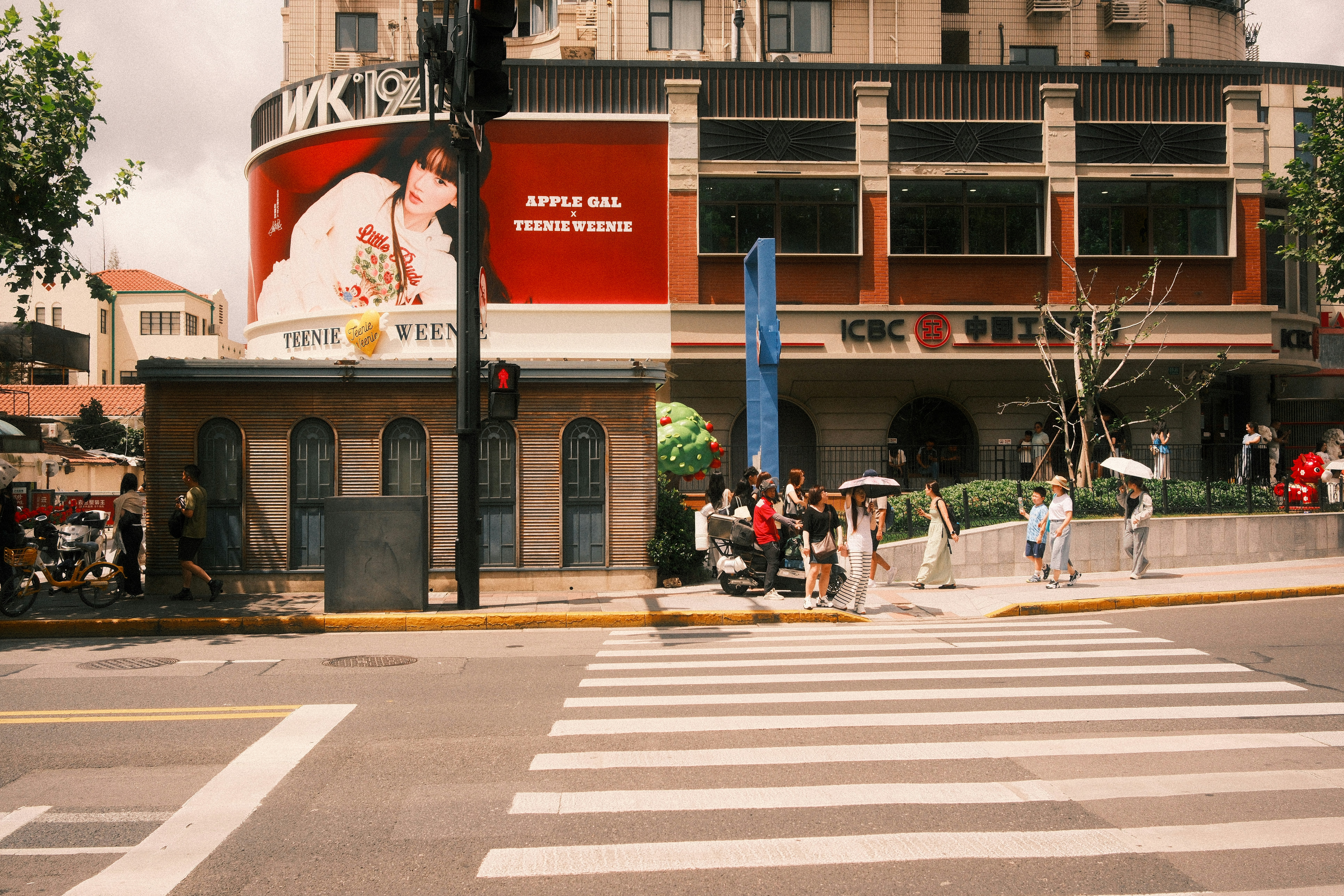 People walking on a sidewalk past a large red advertisement and bank building