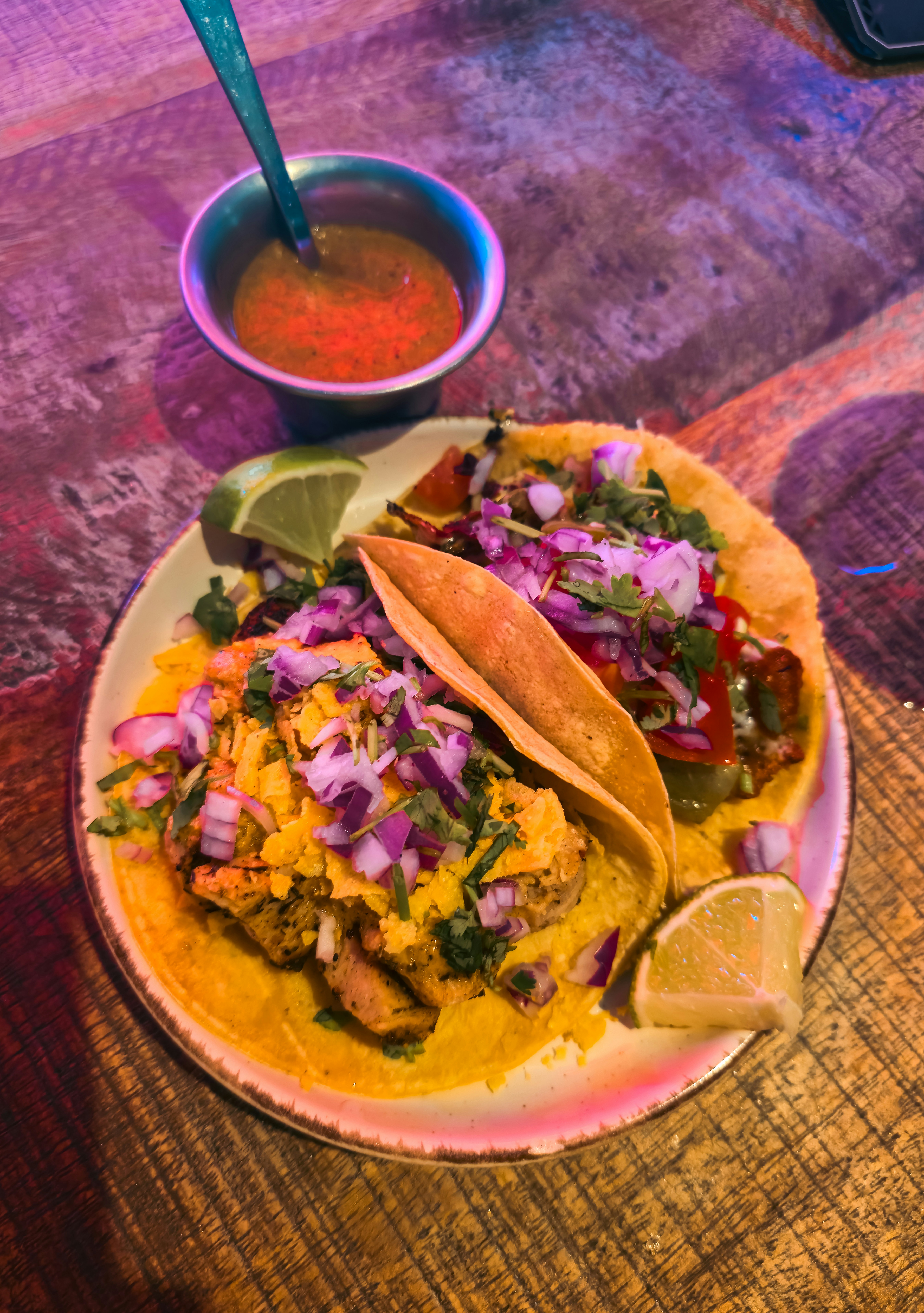 Two tacos with grilled chicken, red onion, and cilantro on a plate with lime