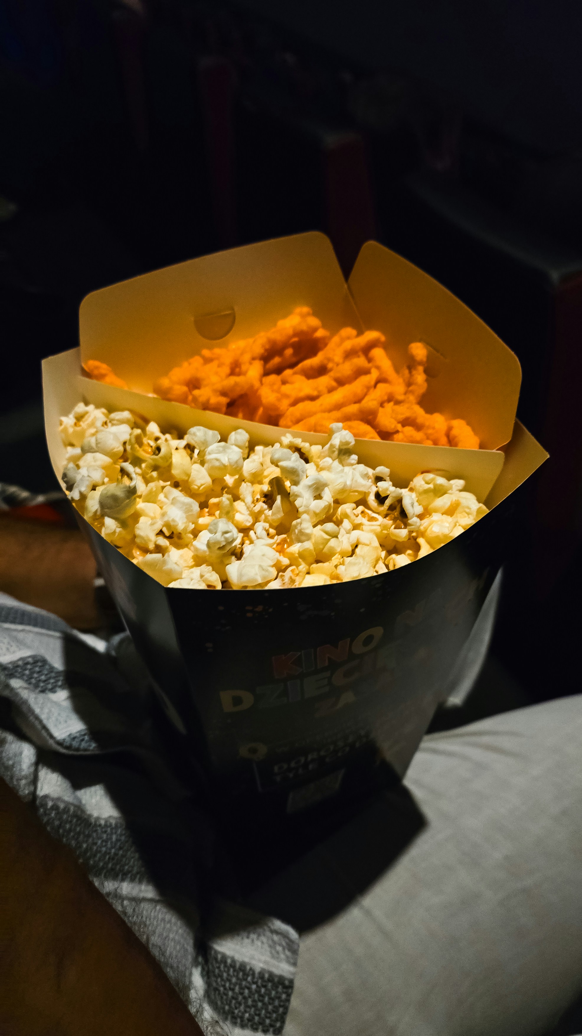 A divided container filled with popcorn and orange cheese snacks in a dark theater