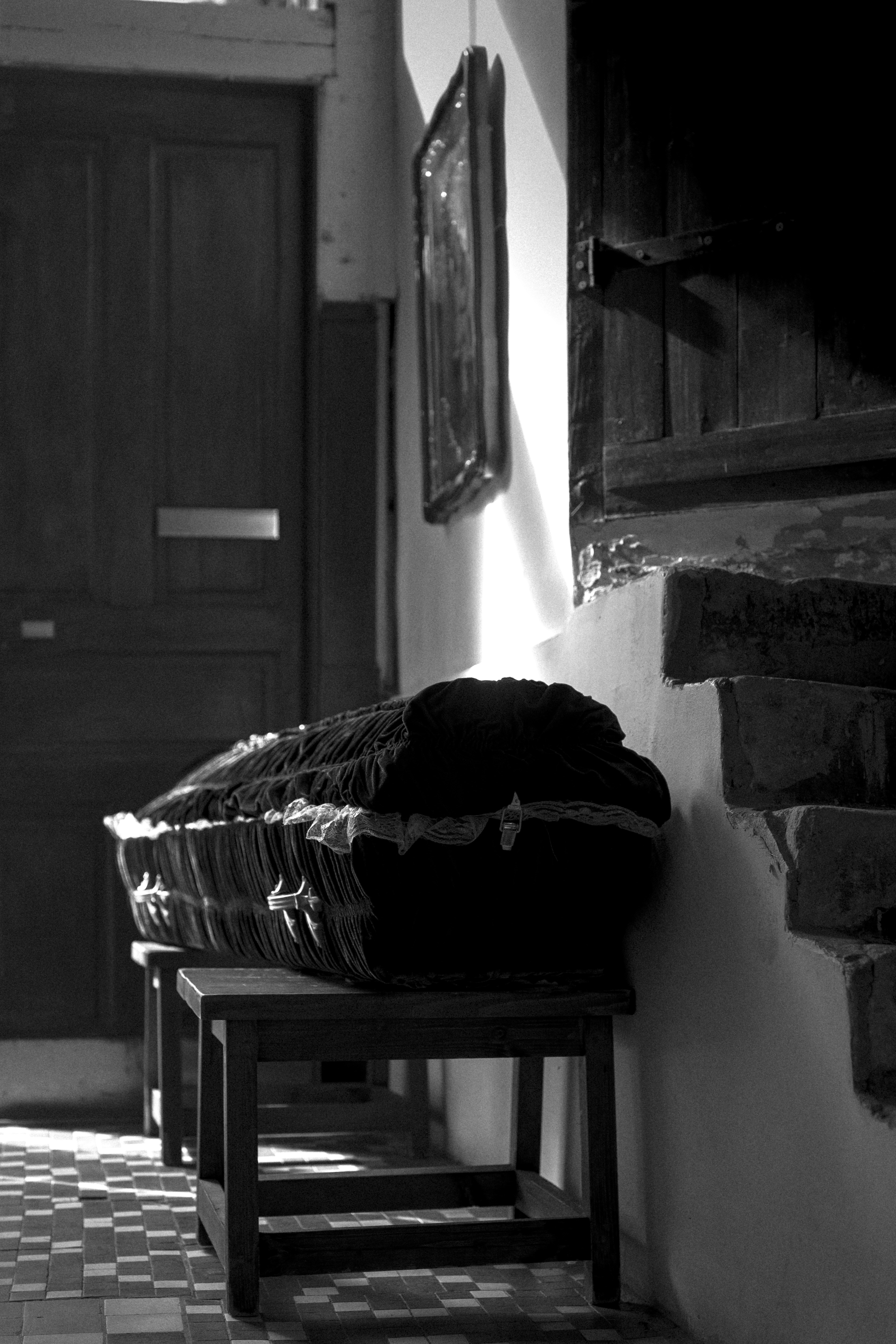 A black velvet casket on wooden stools in a sunlit hallway