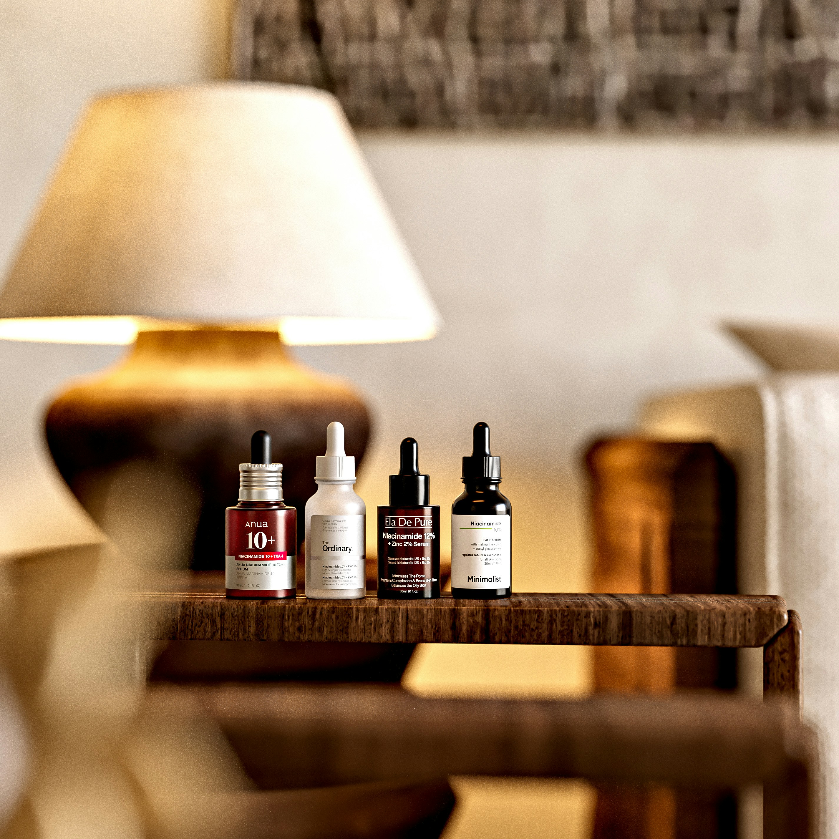 Four glass dropper bottles of facial serum on a wooden surface with a lamp