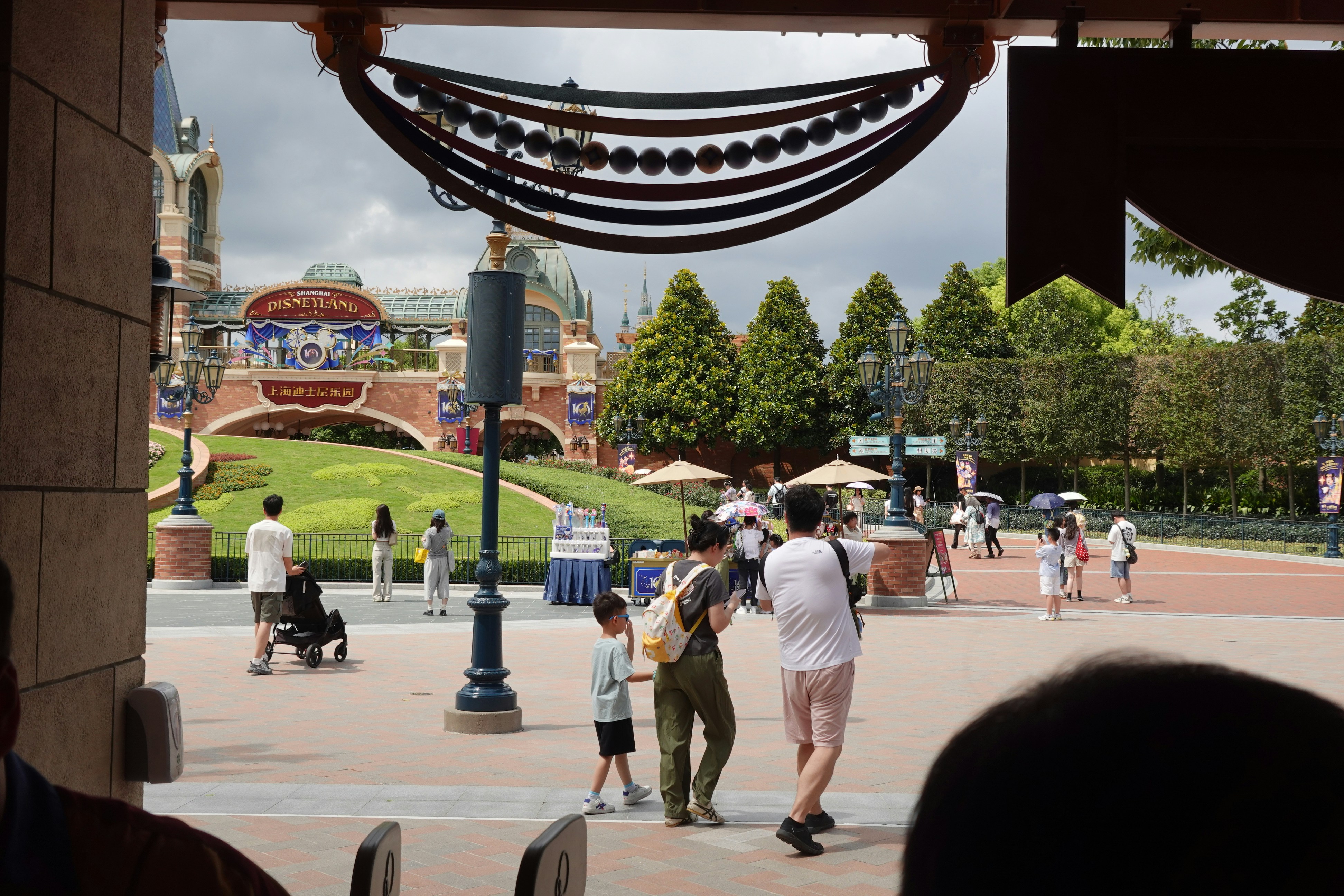 装飾的なアーチのある上海ディズニーランドの入口広場を歩く人々