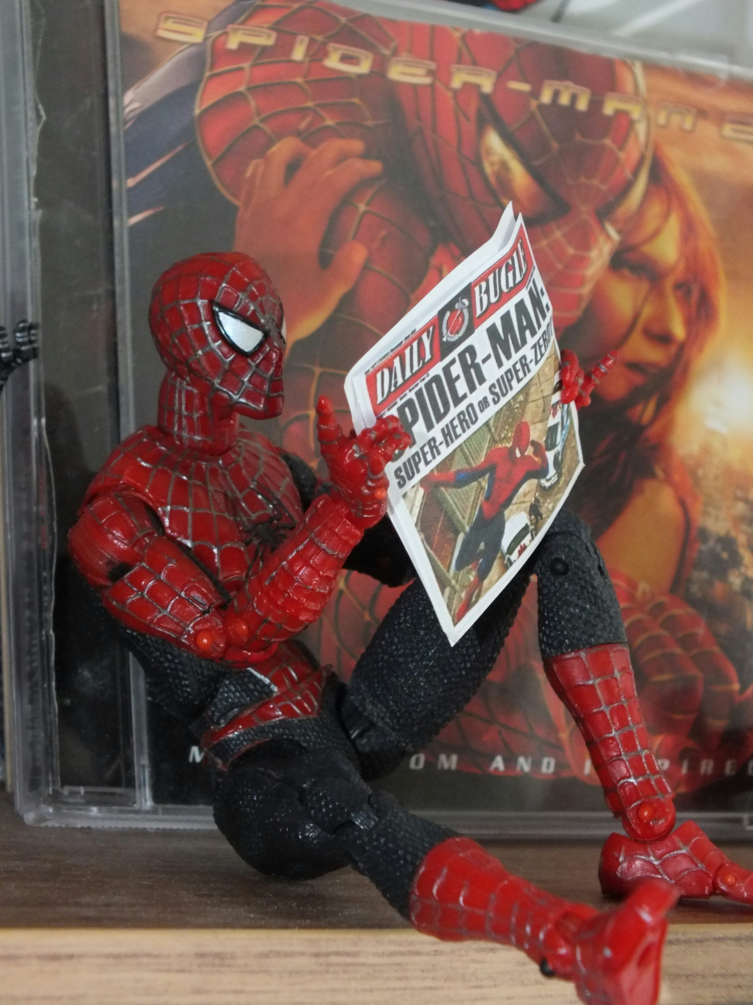 A Spider-Man action figure reading a miniature newspaper in front of a CD case