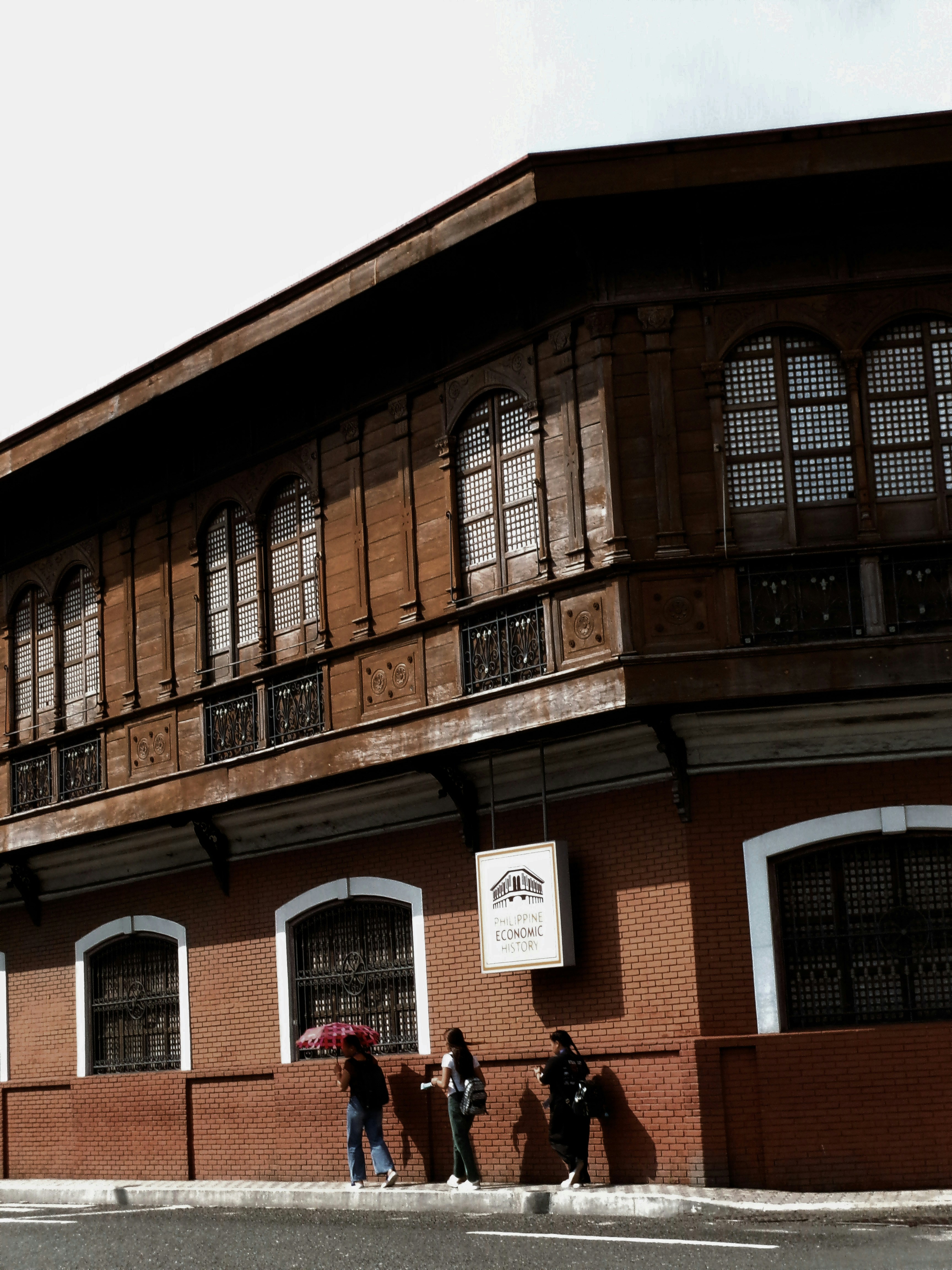 Three people walking past a brick building with a sign reading Philippine Economic History - historical marker hunting