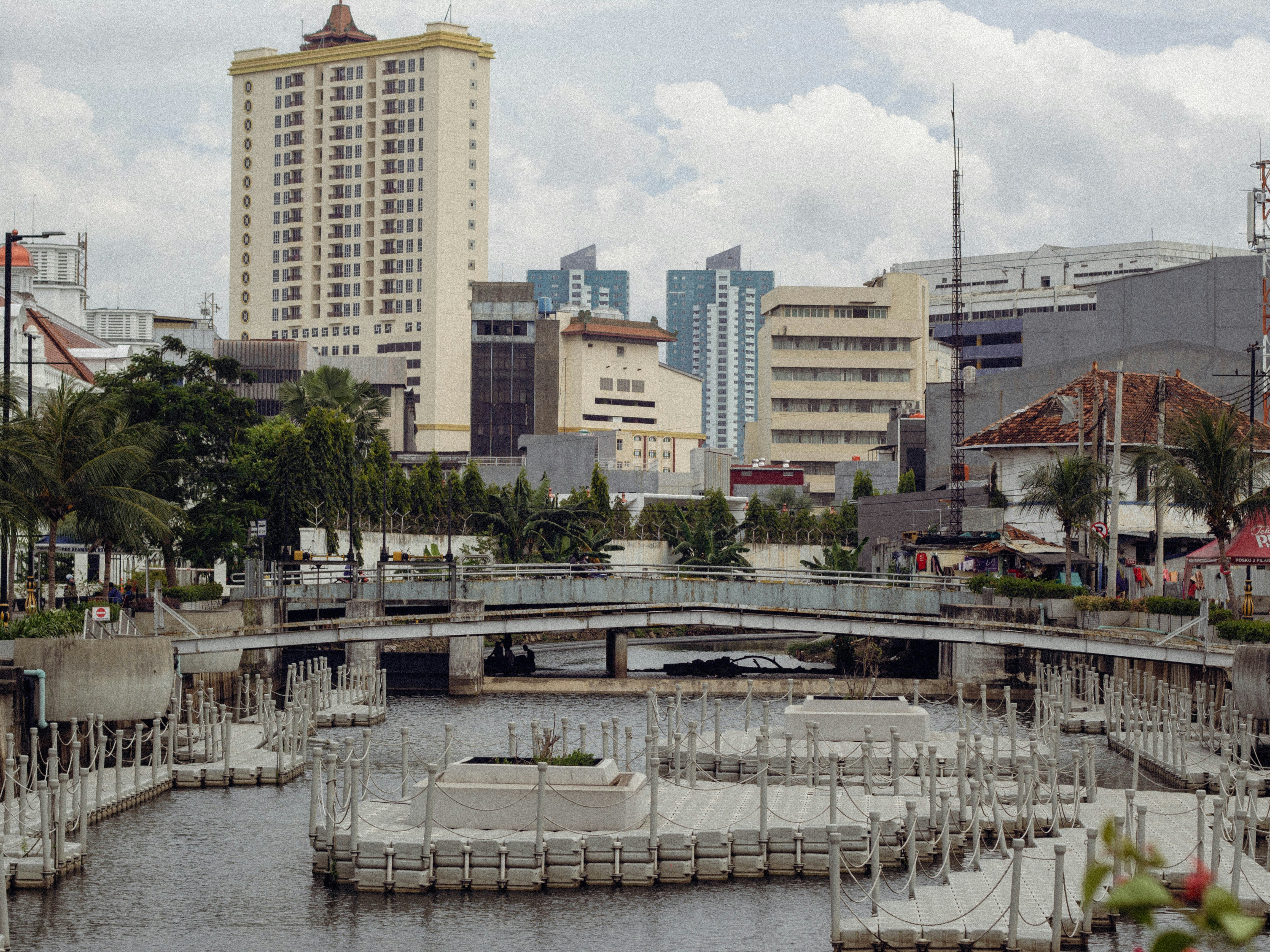 A metal bridge over a canal with floating platforms in Jakarta, Indonesia