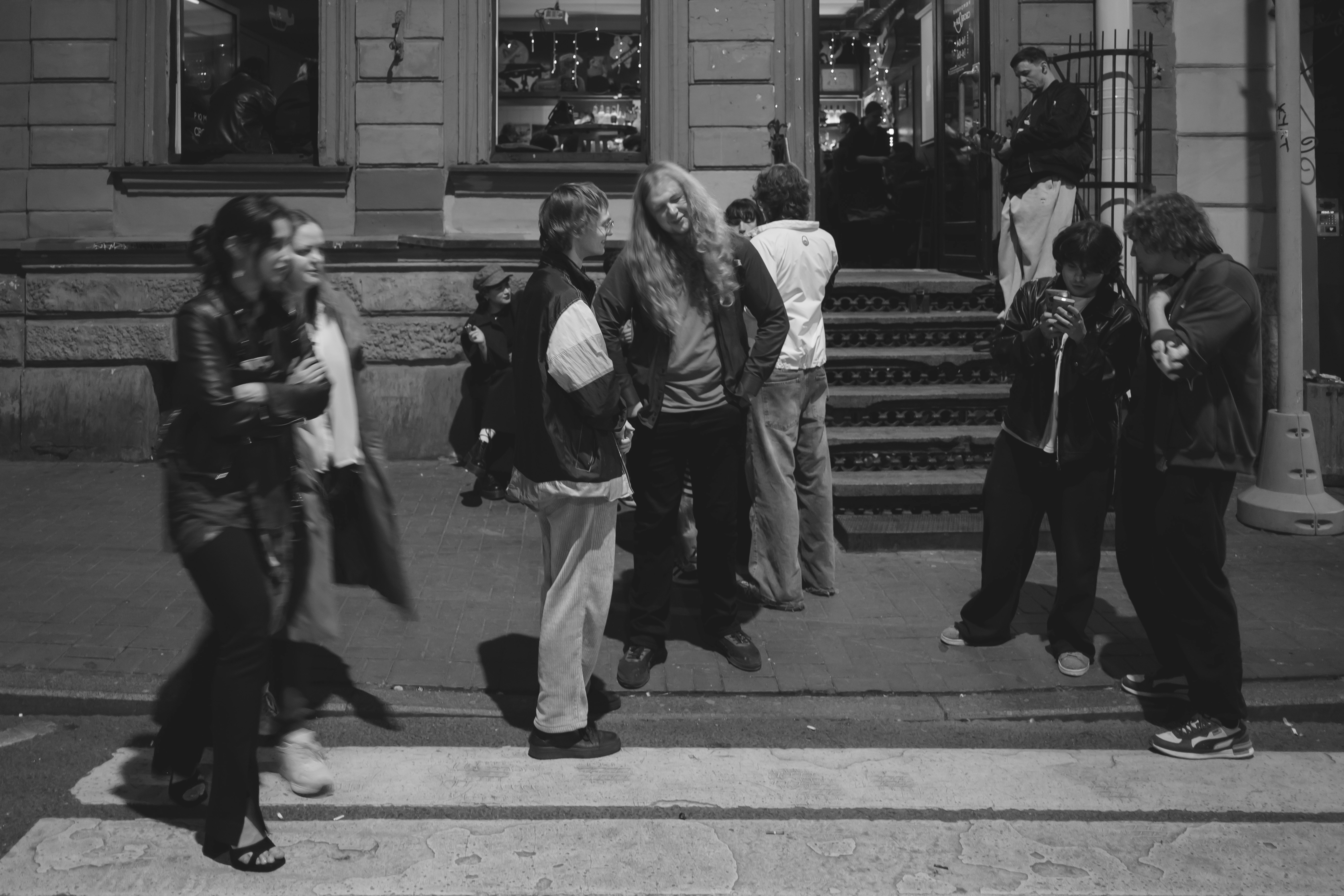A group of people gathered on a sidewalk outside a building at night