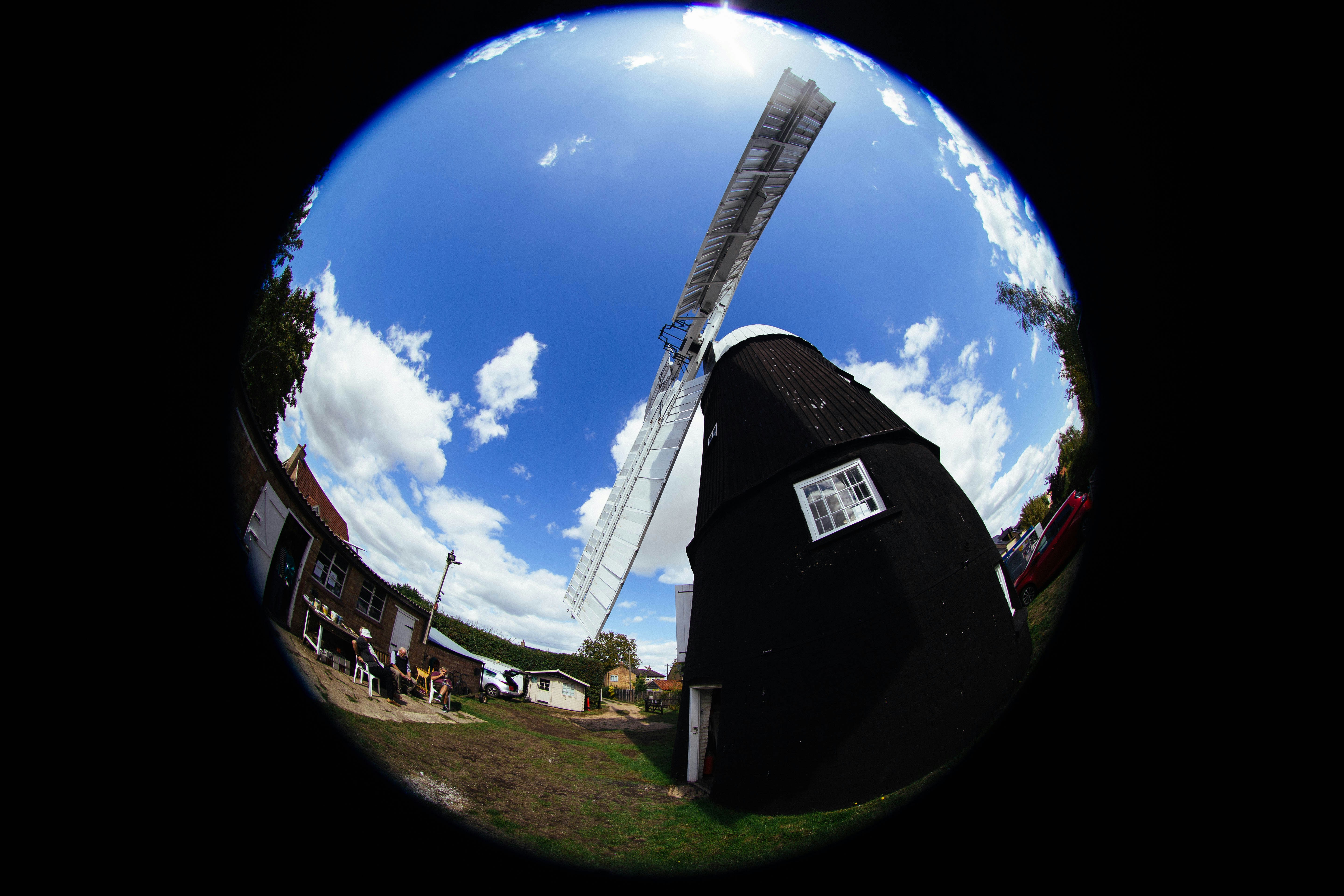A black windmill with white sails under a bright blue sky with clouds