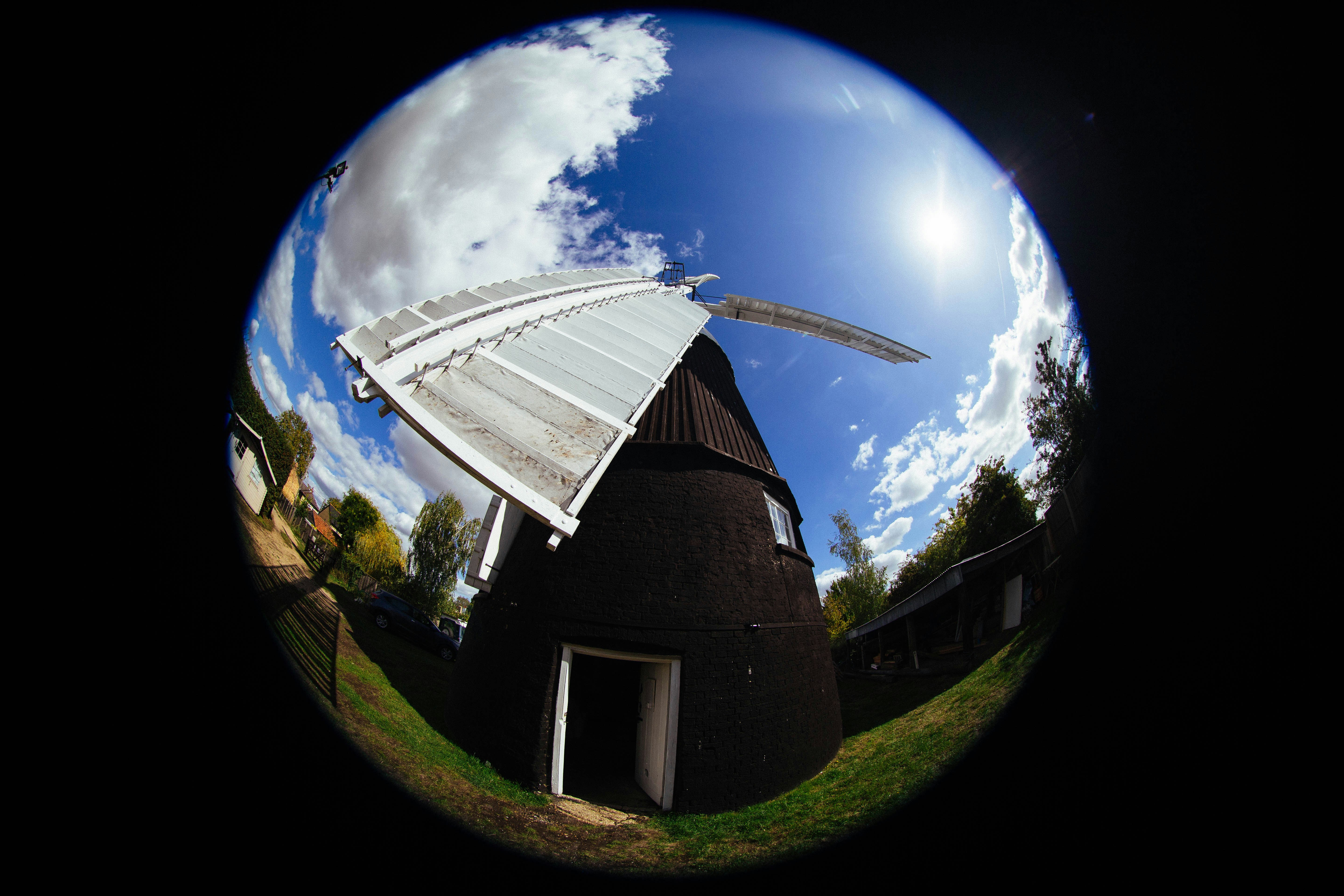 A black windmill with white sails under a bright blue sky with clouds