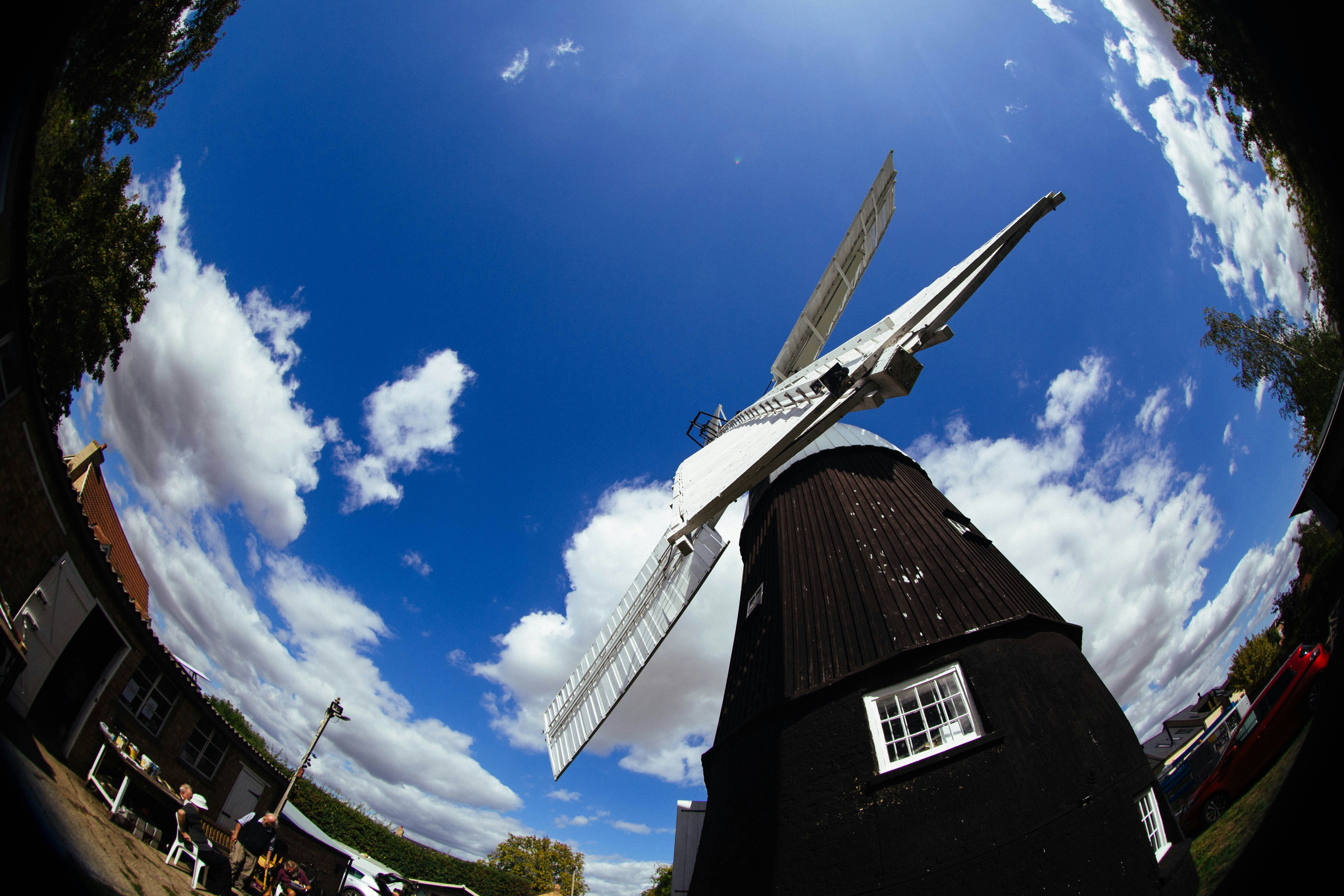 A black windmill with white sails against a bright blue sky with clouds