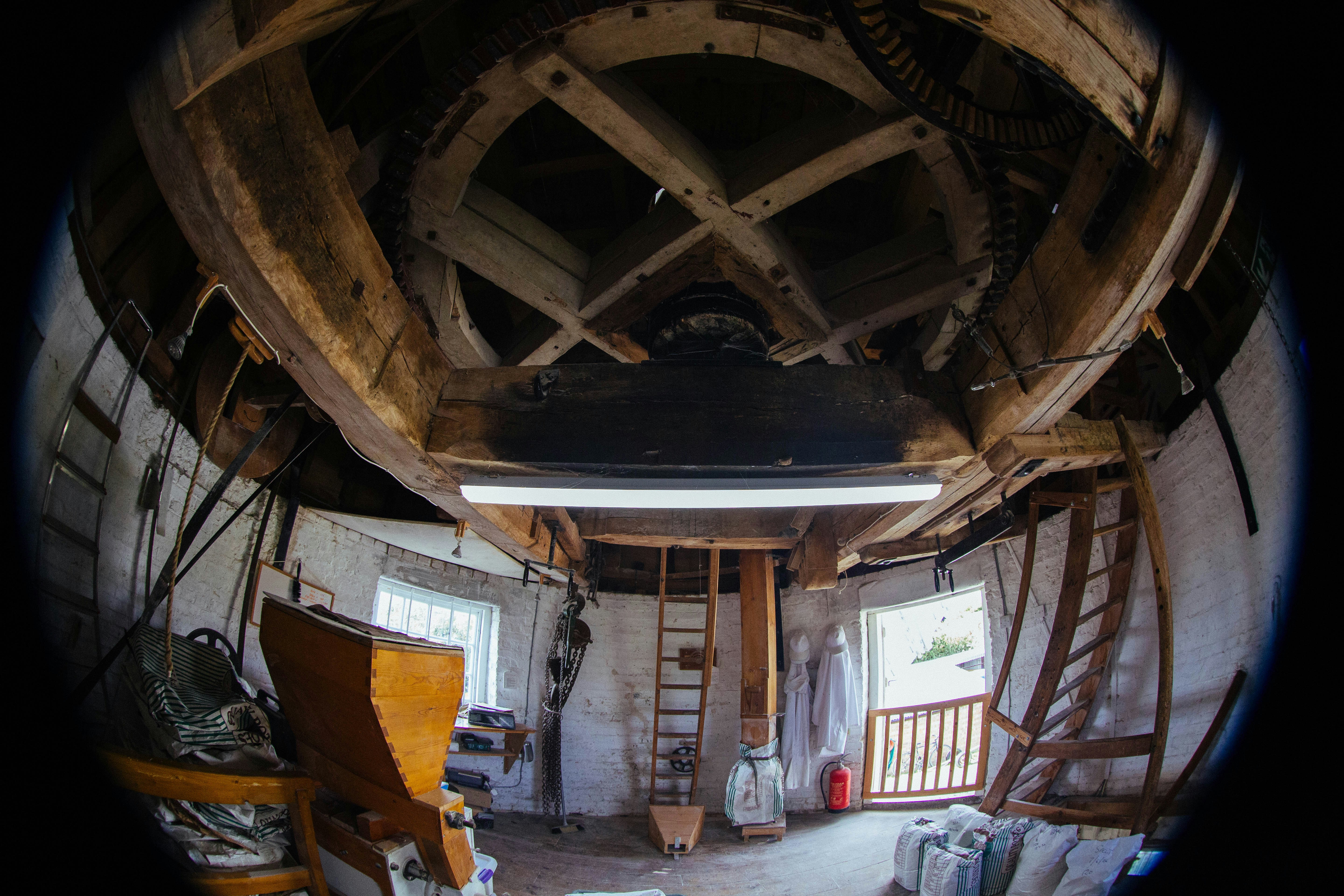 Interior of a windmill with wooden gears, ladders, and white brick walls
