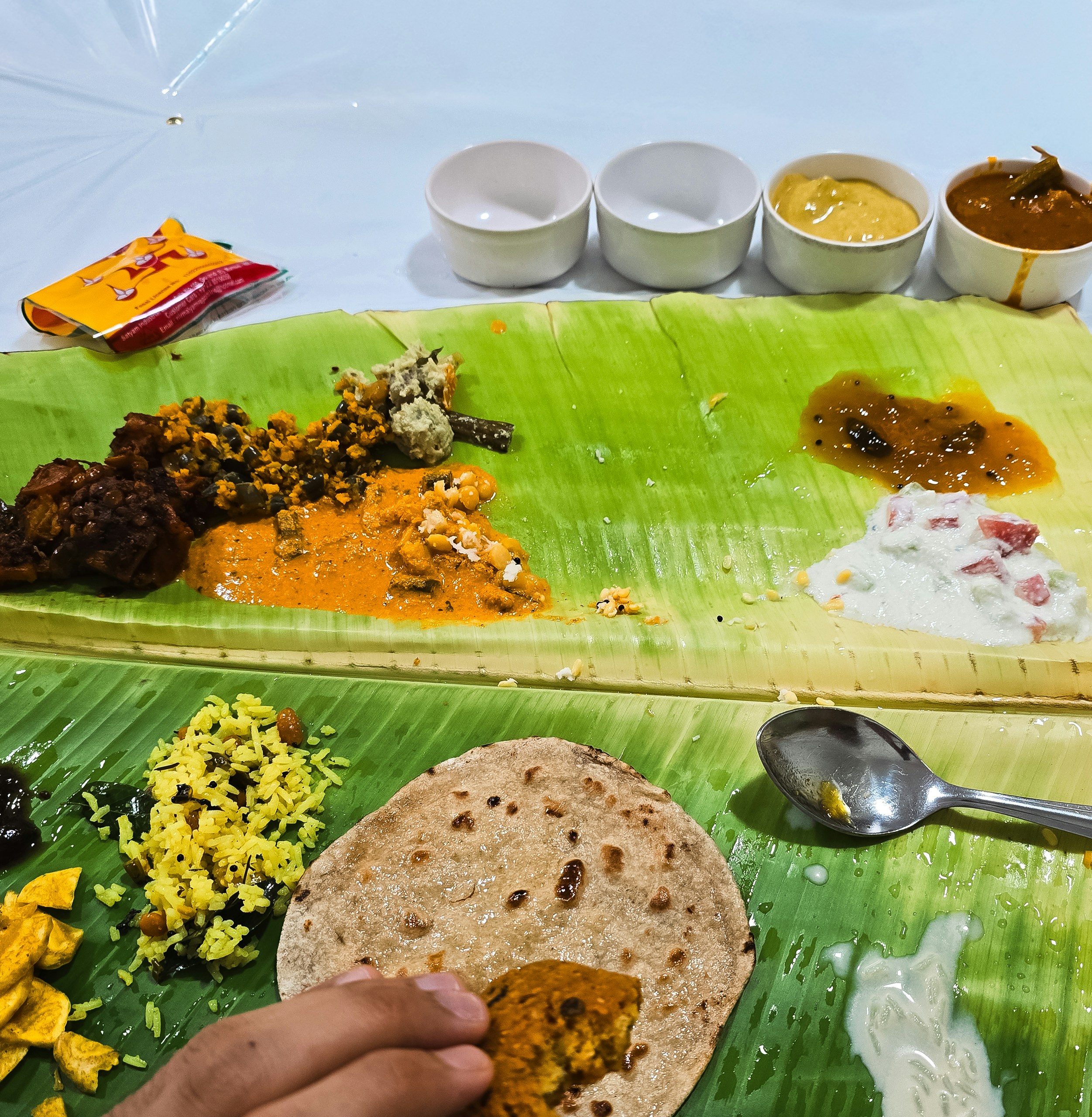 A hand holding food over a traditional Indian meal served on banana leaves